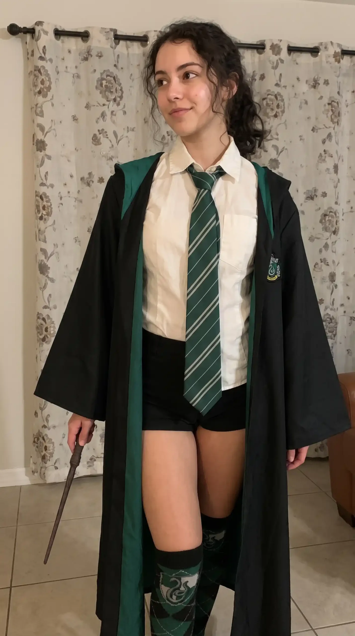Woman dressed as Slytherin student in black Harry Potter robe green trim white shirt striped tie Slytherin knee socks and wand