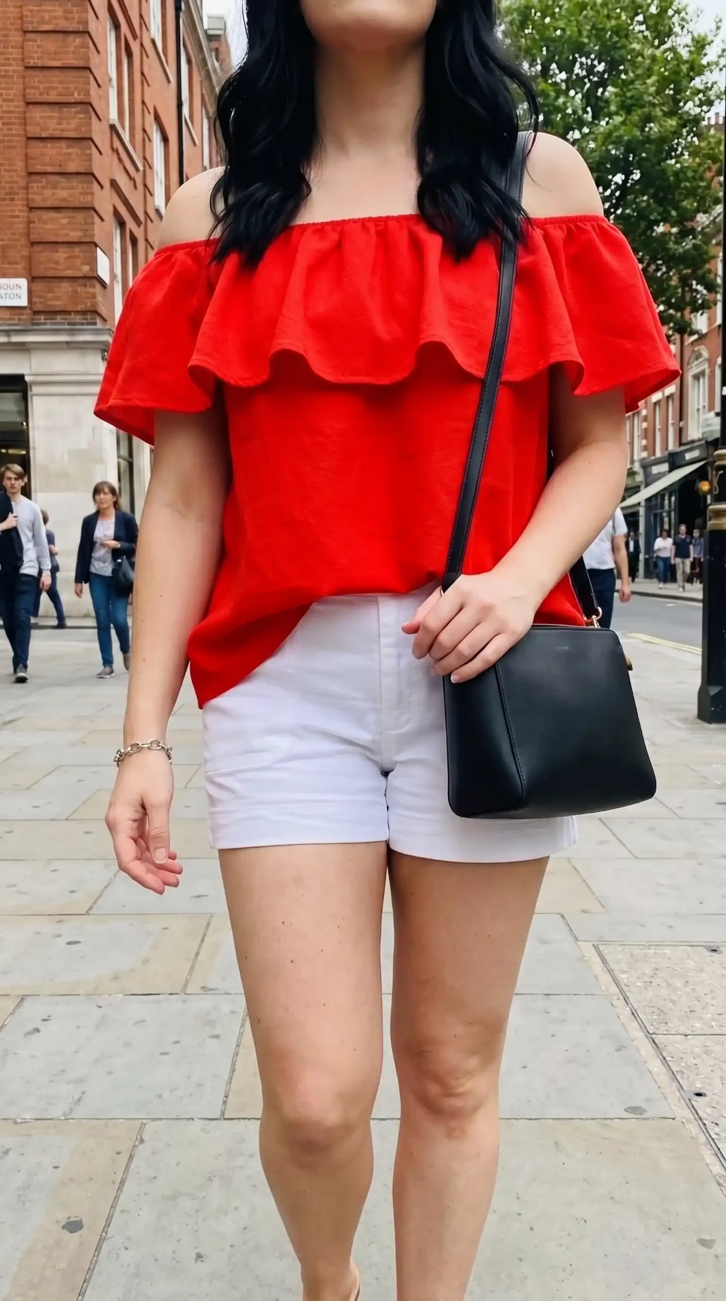 Woman wearing red ruffle off shoulder top with white high waist denim shorts on London city street