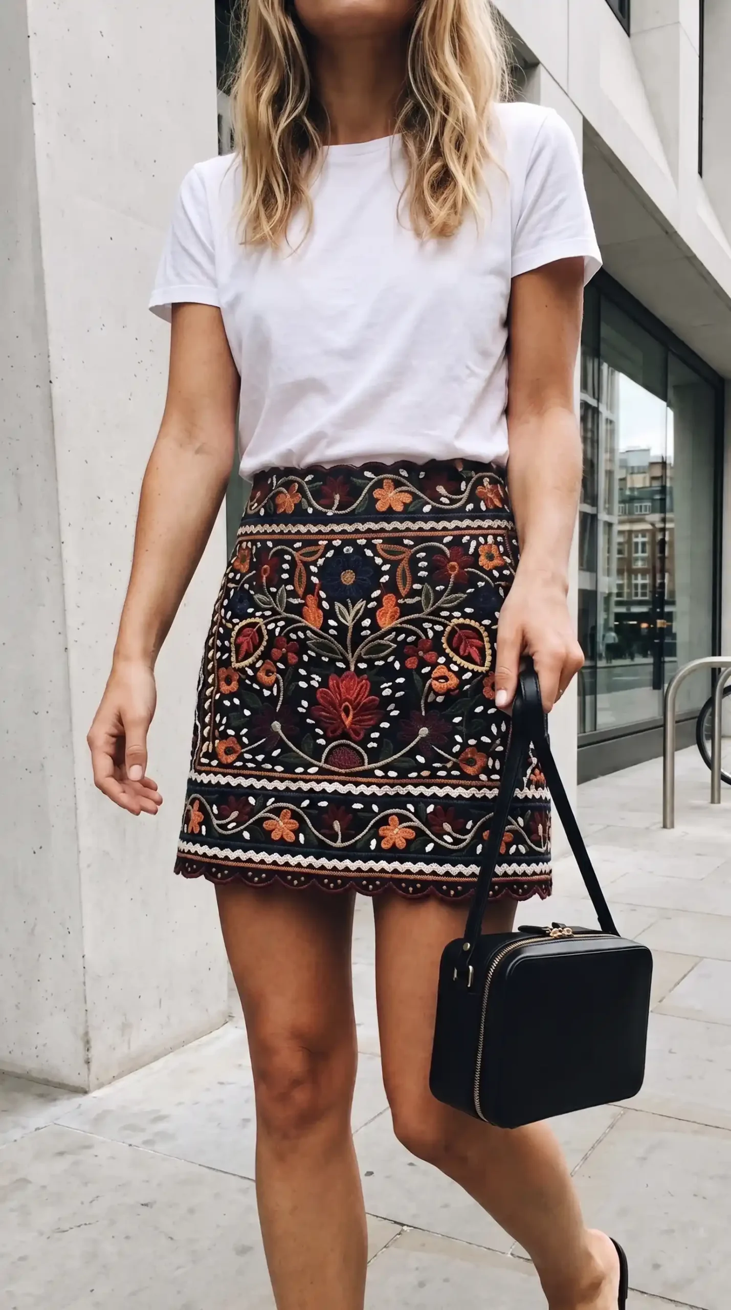 Woman wearing white crew neck t shirt with black multicolor floral embroidered scallop hem mini skirt on city street