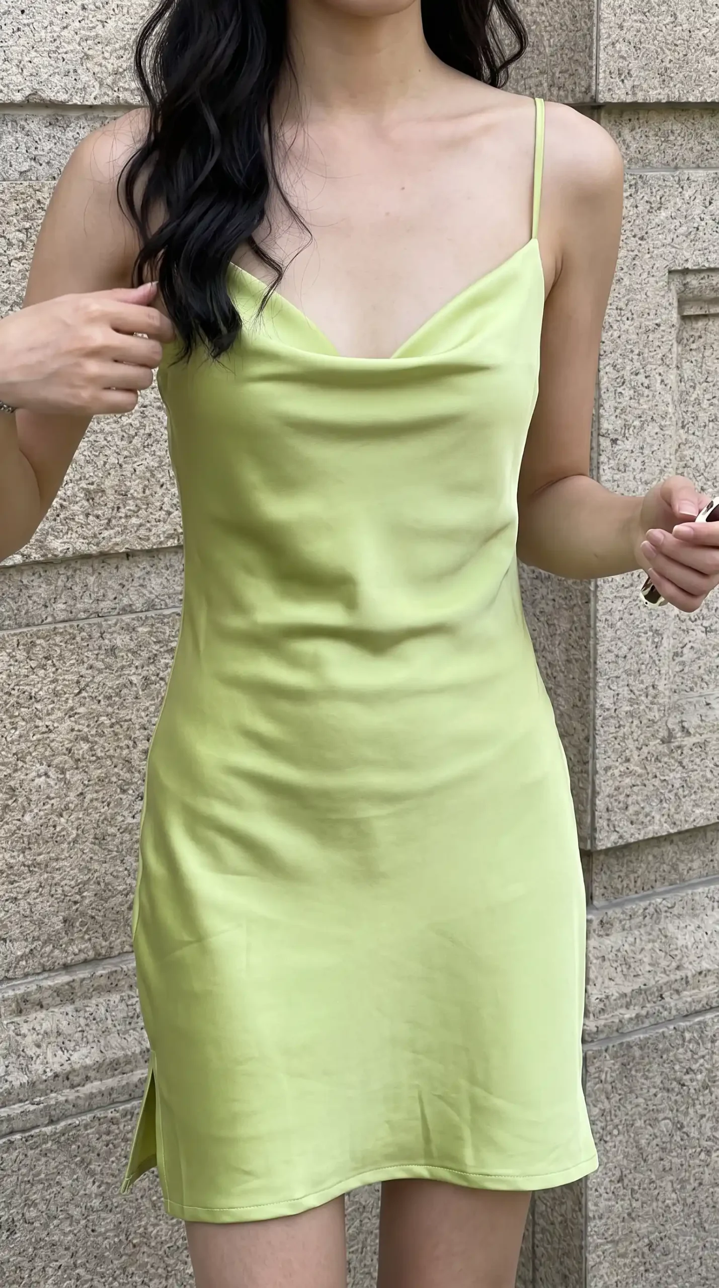 Lime green satin cowl neck spaghetti strap mini slip dress against stone wall