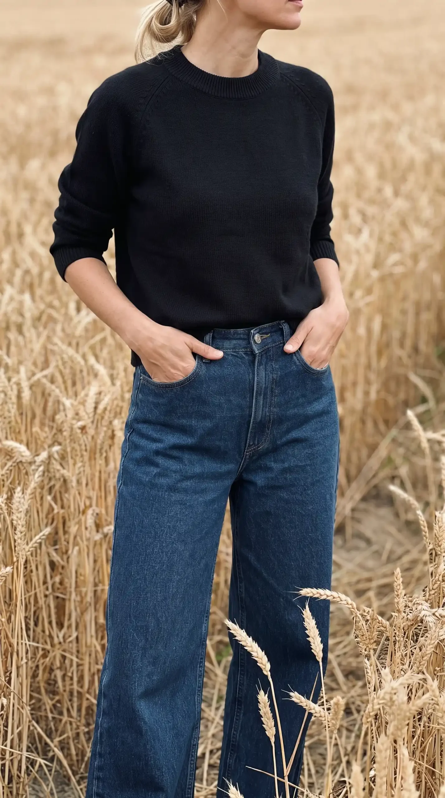 Woman wearing navy knit sweater with mid blue wide leg jeans in wheat field