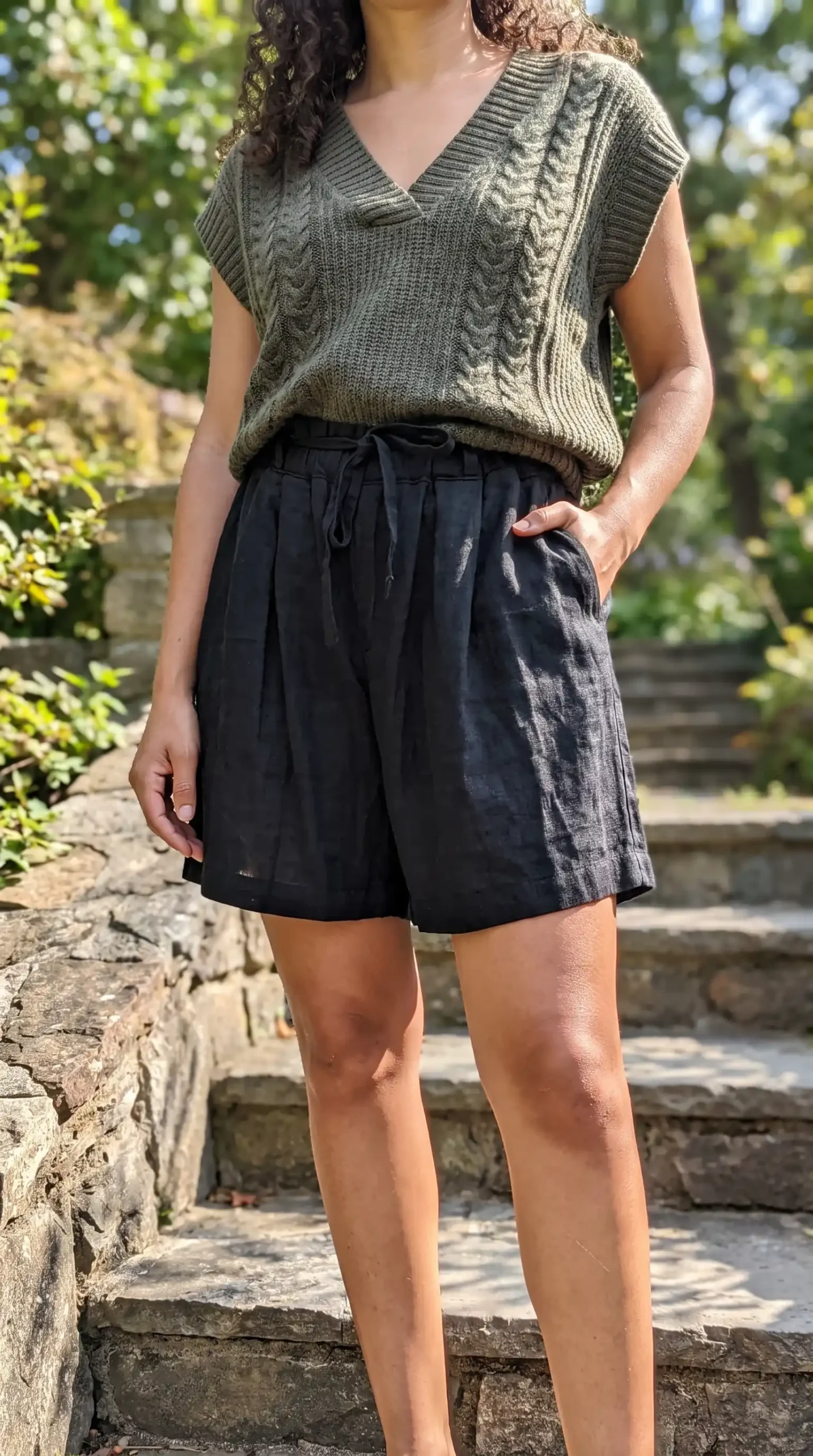 Woman wearing olive green cable knit vest with black linen drawstring shorts outdoors