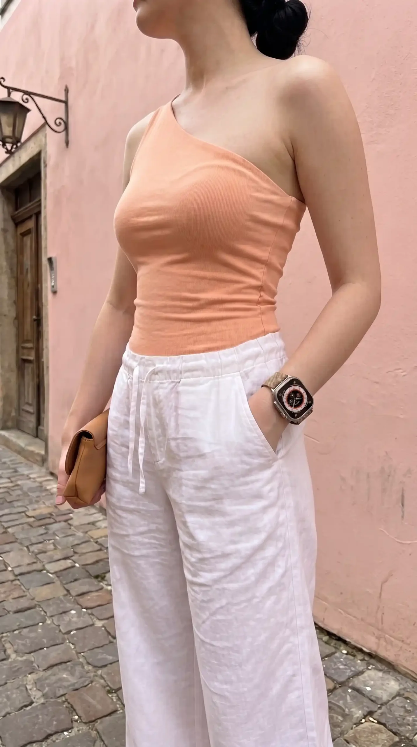 Woman wearing peach one shoulder ribbed top with white linen wide leg trousers on cobblestone street