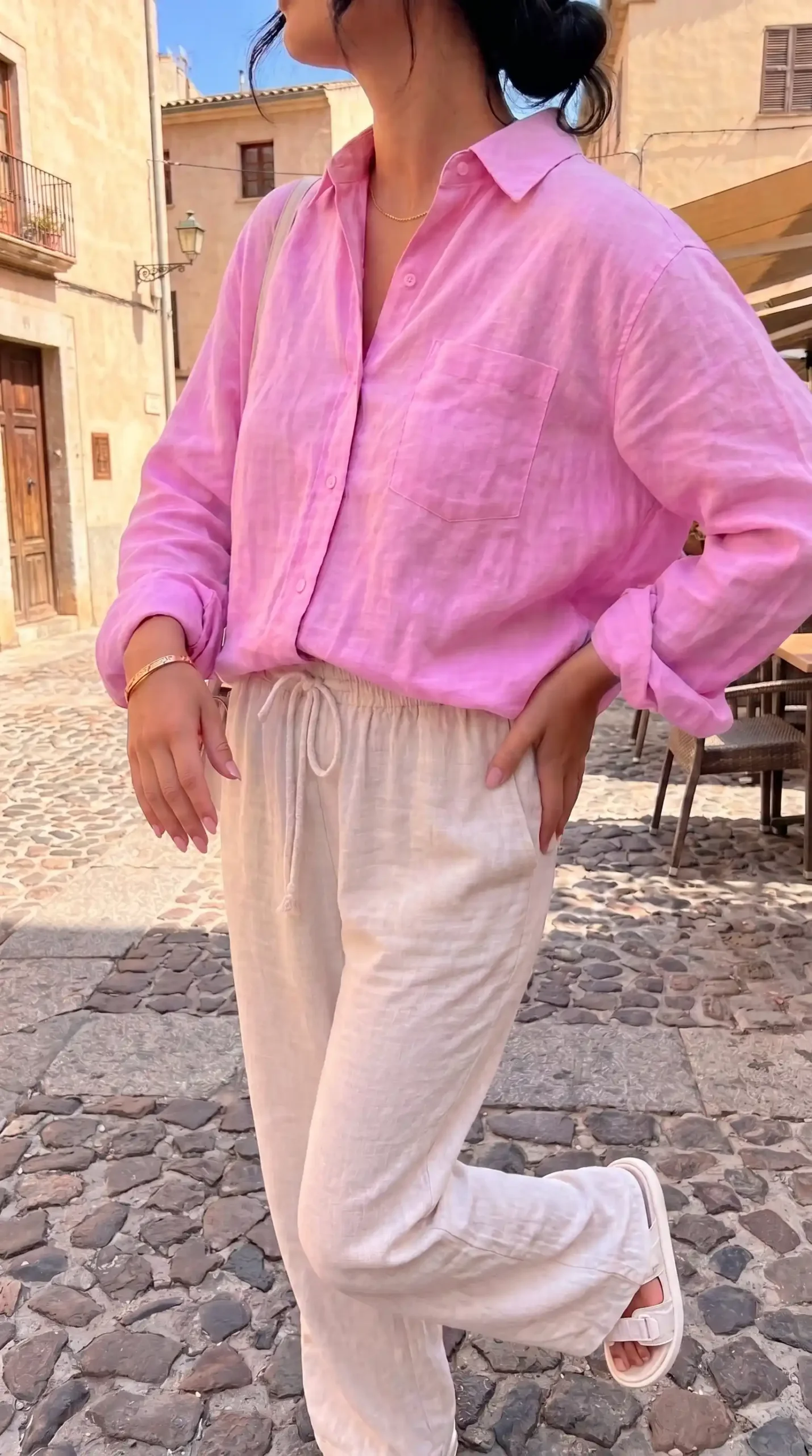 Woman wearing pink oversized linen shirt with cream linen trousers on European cobblestone street