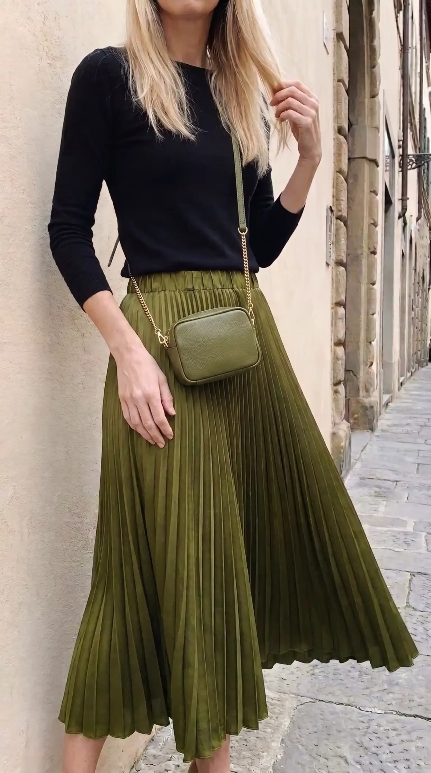 Woman in black knit top with olive green pleated midi skirt on cobblestone street