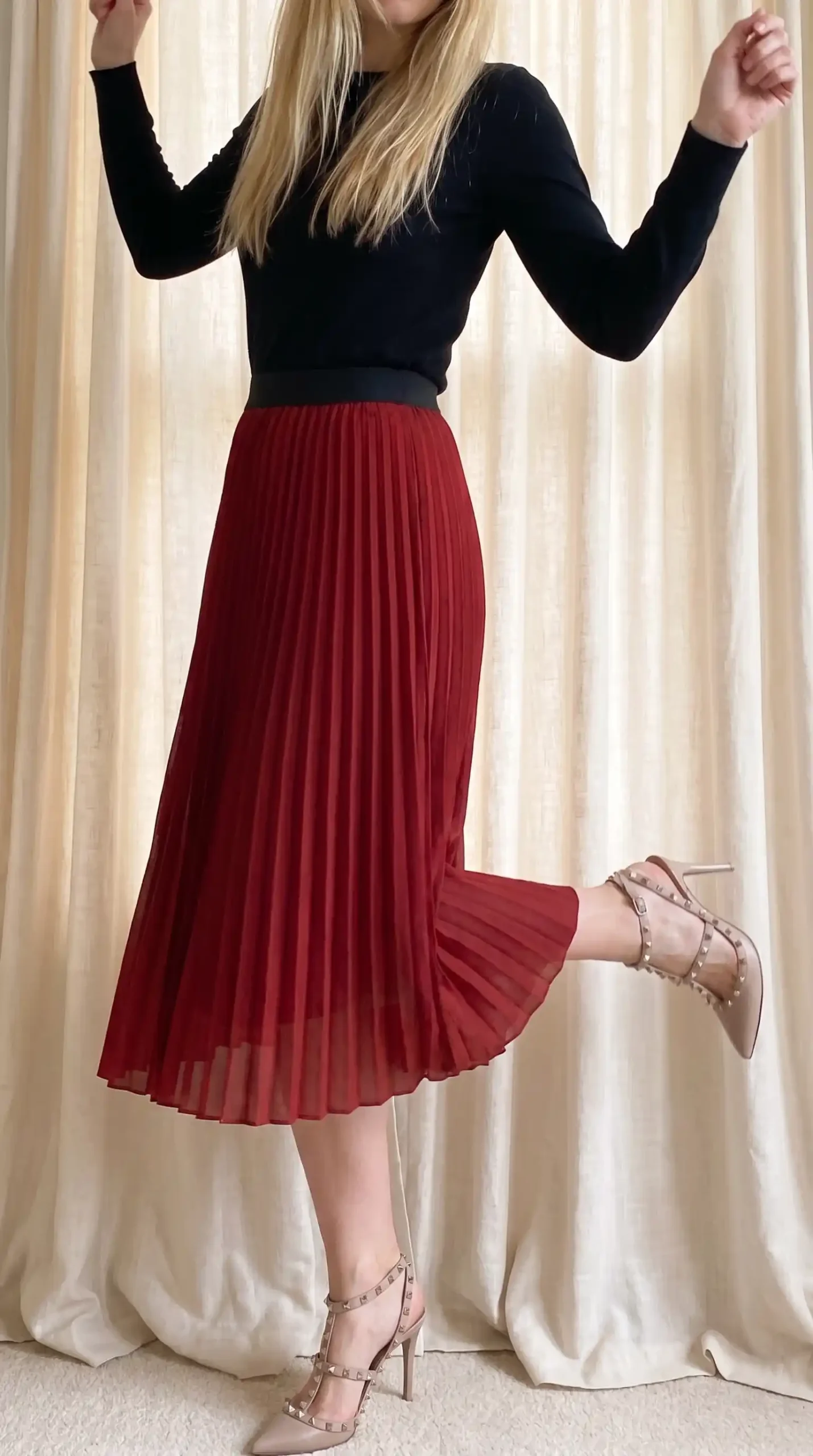 Woman in black long sleeve top with dark red pleated chiffon midi skirt and nude studded heels