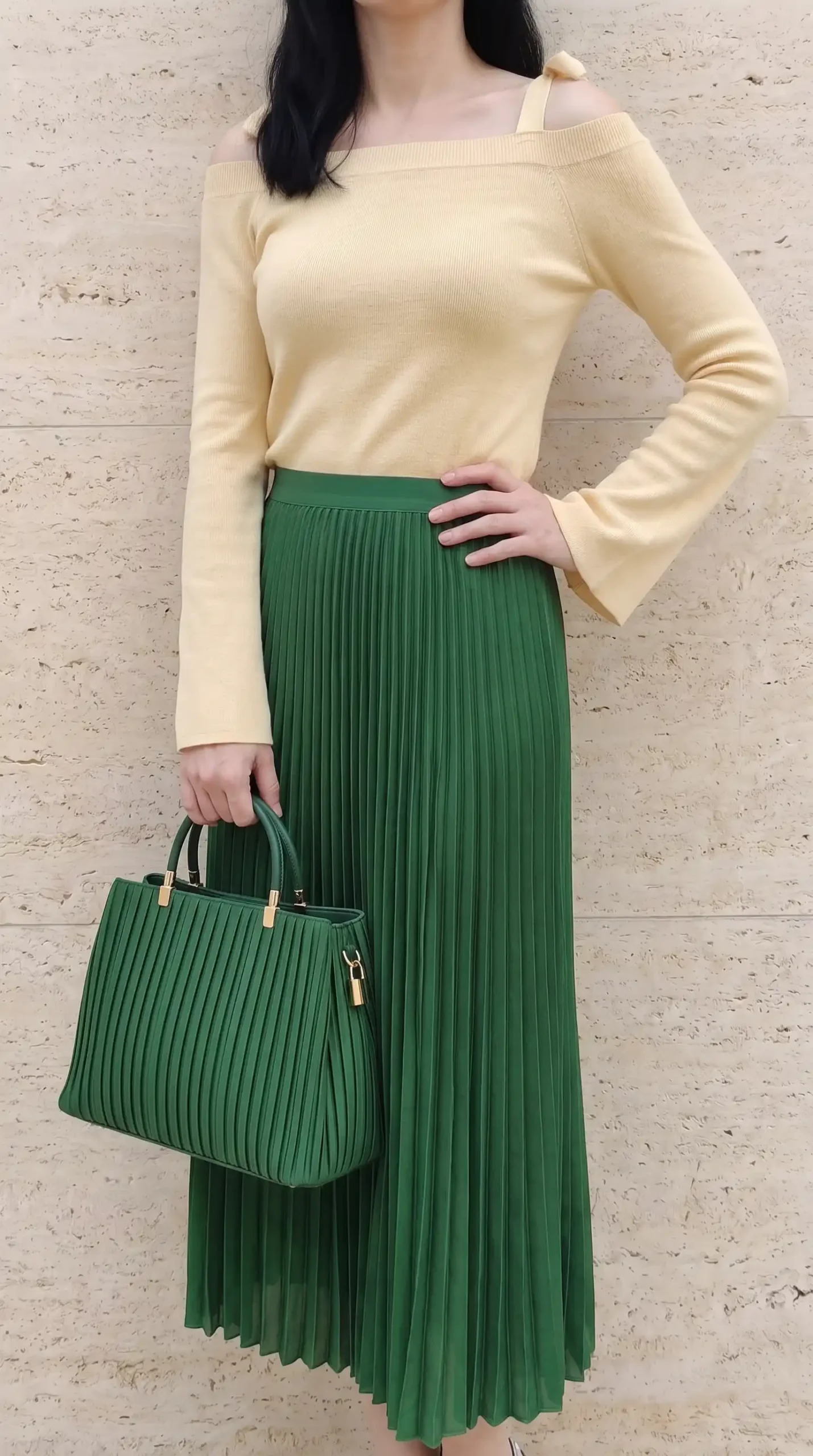 Woman in butter yellow off shoulder ribbed knit top with emerald green pleated midi skirt