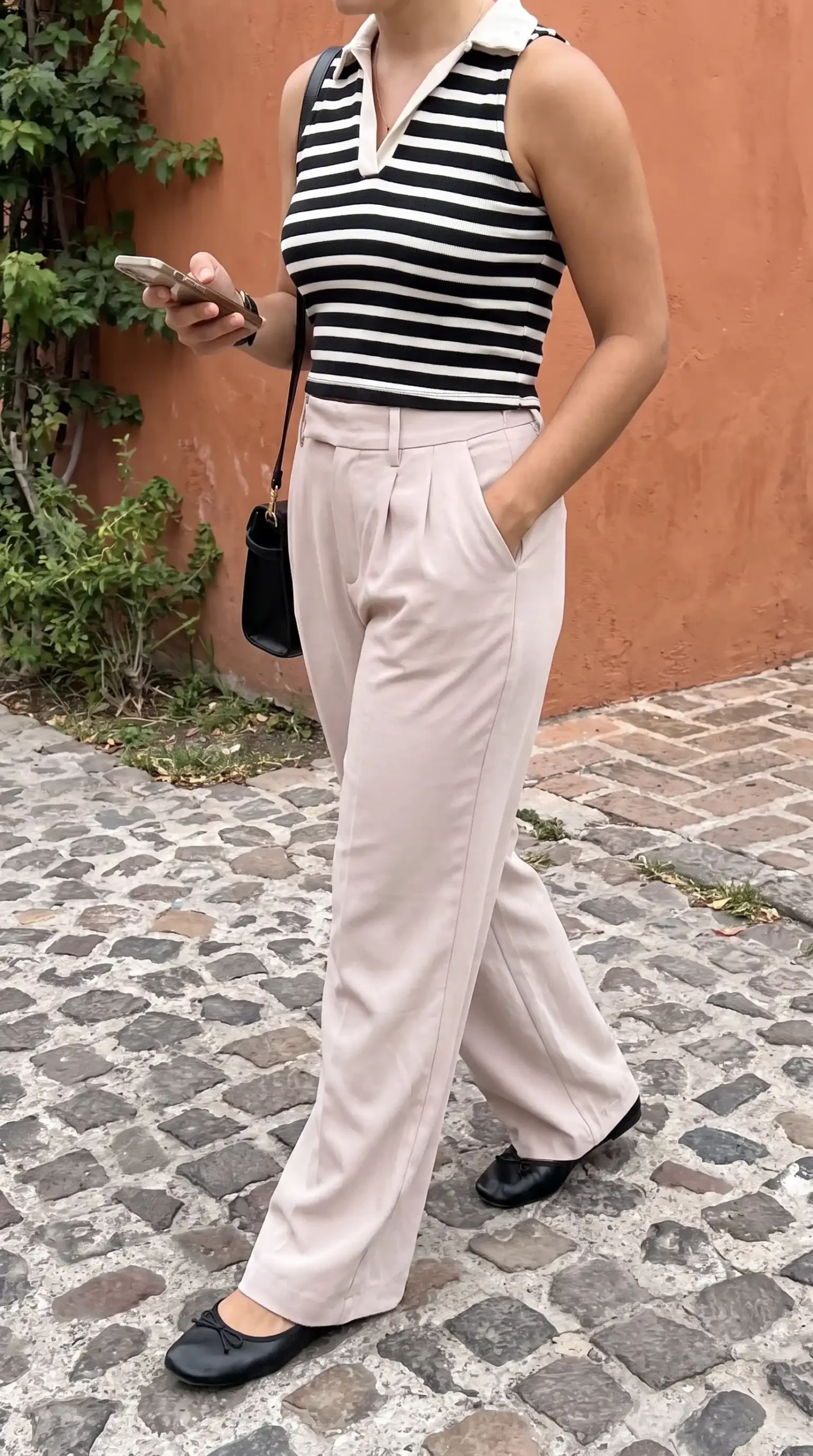 Woman wearing black white stripe polo knit top with blush wide leg trousers on cobblestone street