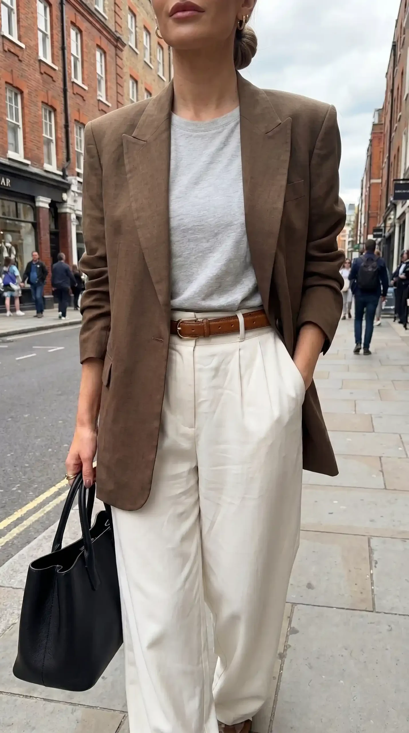 Woman wearing brown blazer with grey tee cream wide leg trousers and tan belt outdoors