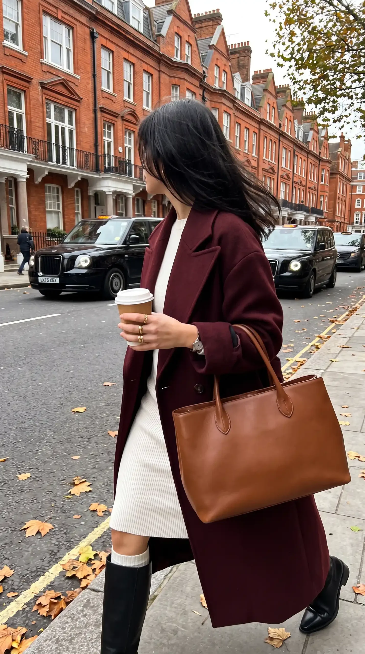 Woman wearing burgundy wool coat over cream ribbed knit dress with black knee high boots outdoors