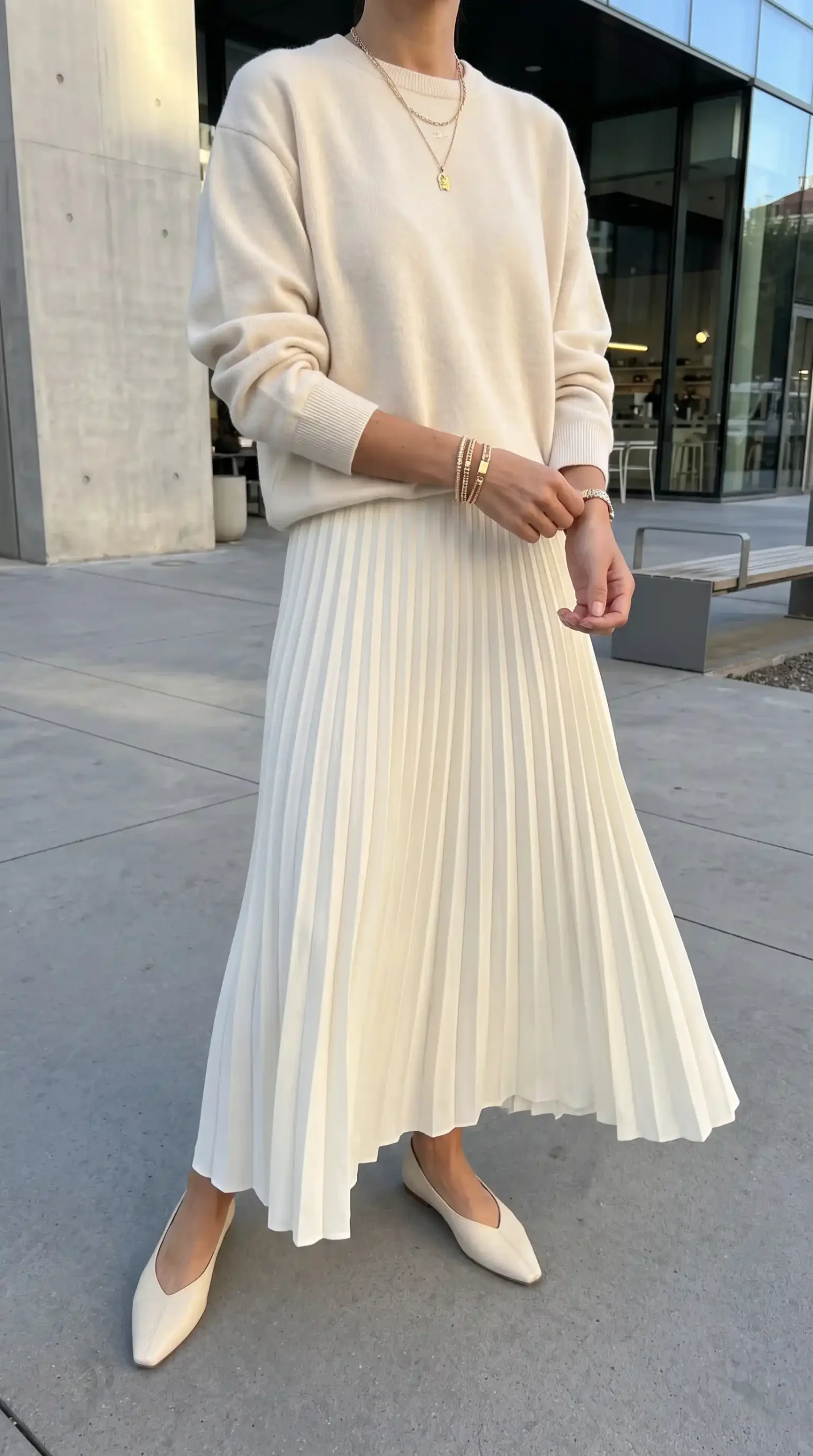 Woman wearing cream oversized knit sweater with cream pleated maxi skirt and cream pointed flats outdoors