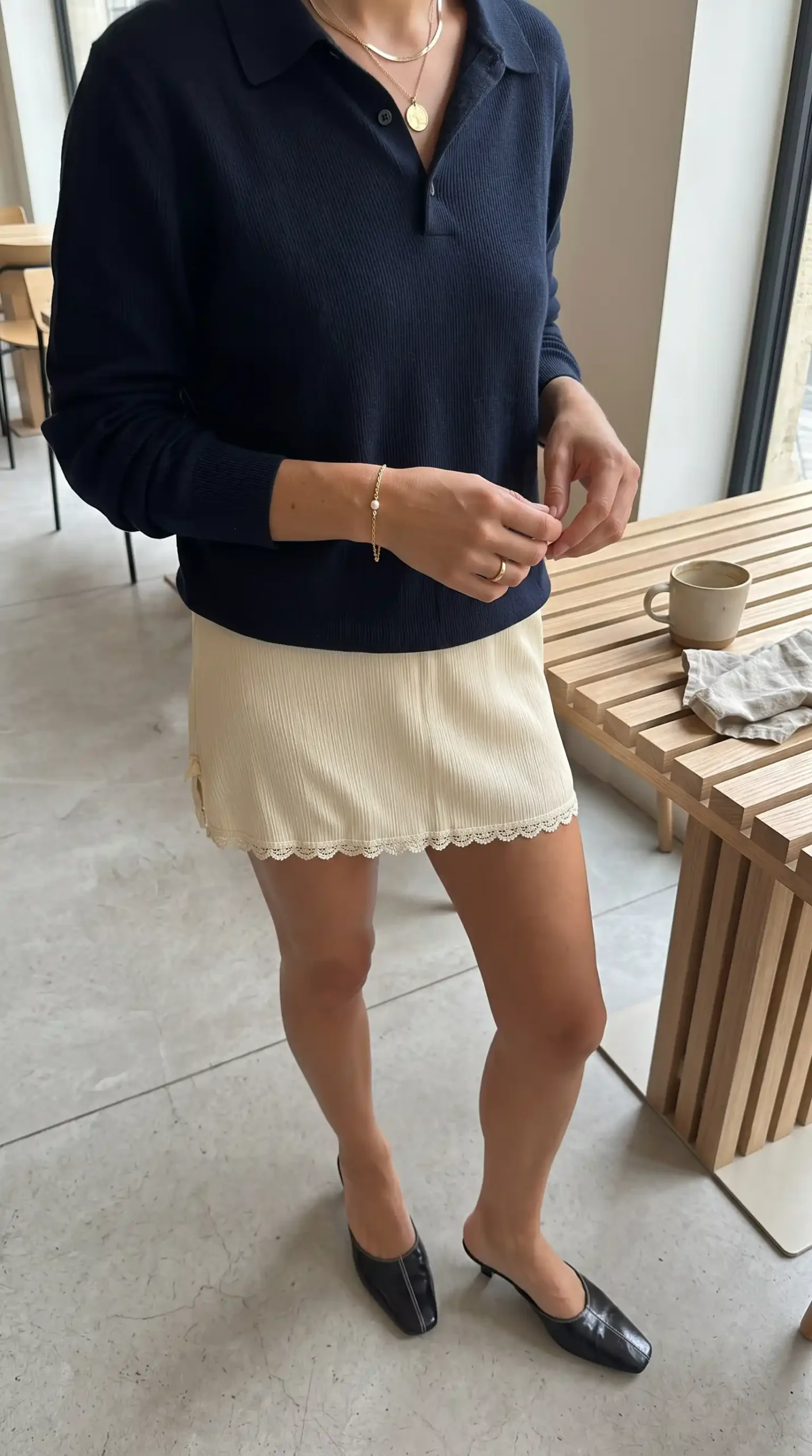 Woman wearing navy ribbed polo knit top with cream lace hem mini skirt and black kitten heel mules indoors