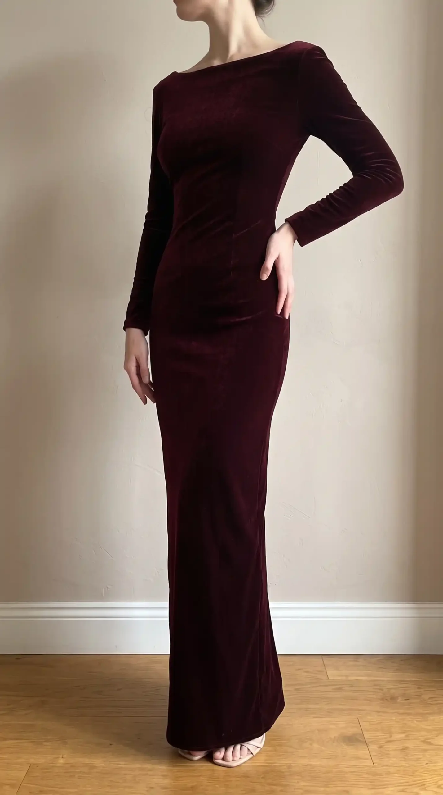 Woman wearing deep burgundy velvet bateau neck long sleeve fitted maxi dress with nude strappy heels