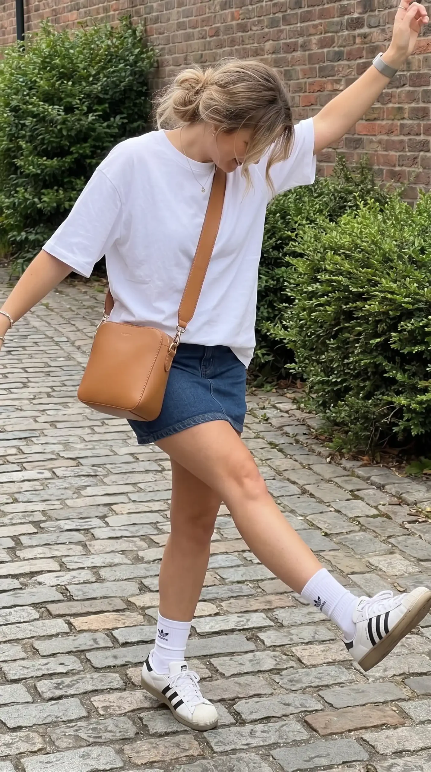 Woman wearing white oversized tee and denim mini skirt with white sneakers on cobblestone street