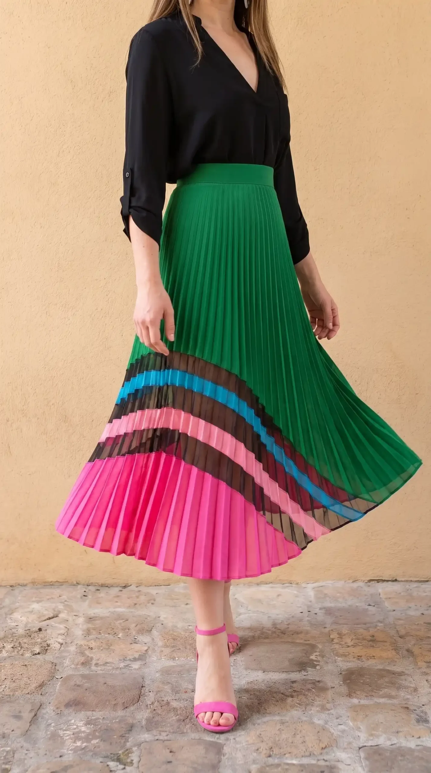 Woman in black v neck blouse with green pink blue colourblock pleated midi skirt and hot pink heels