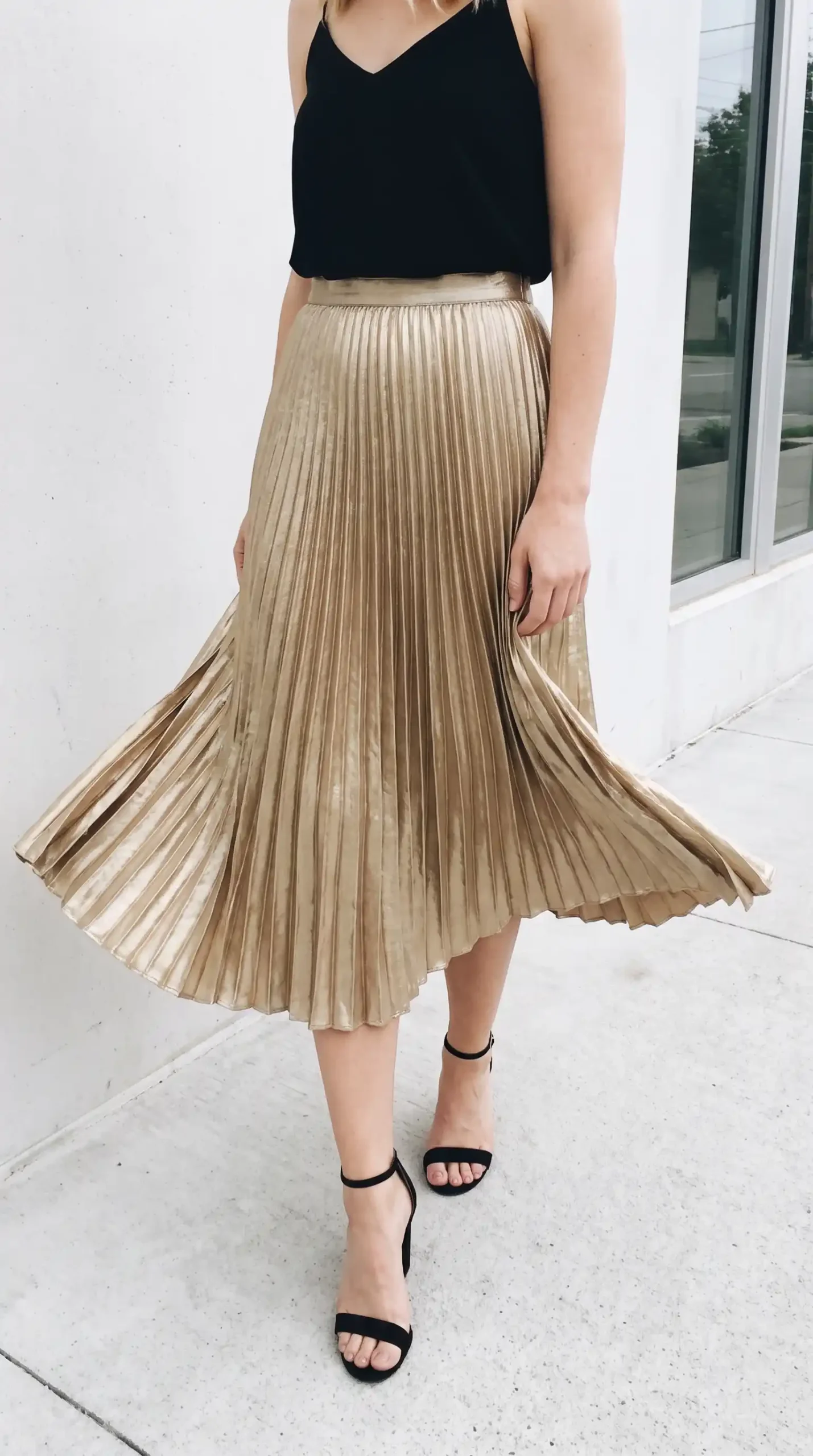 Woman in black satin cami with gold metallic pleated midi skirt and black strappy heels
