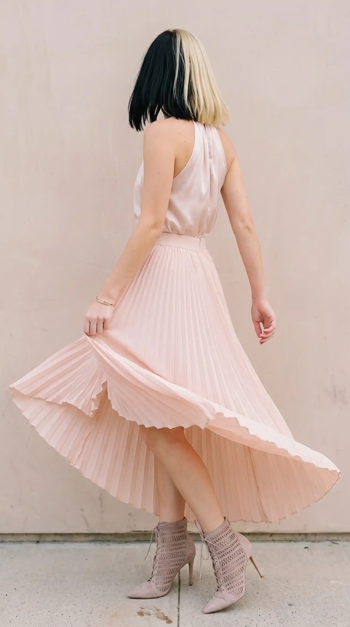 Woman in blush pink satin halter top with blush pleated maxi skirt and nude lace up heeled booties