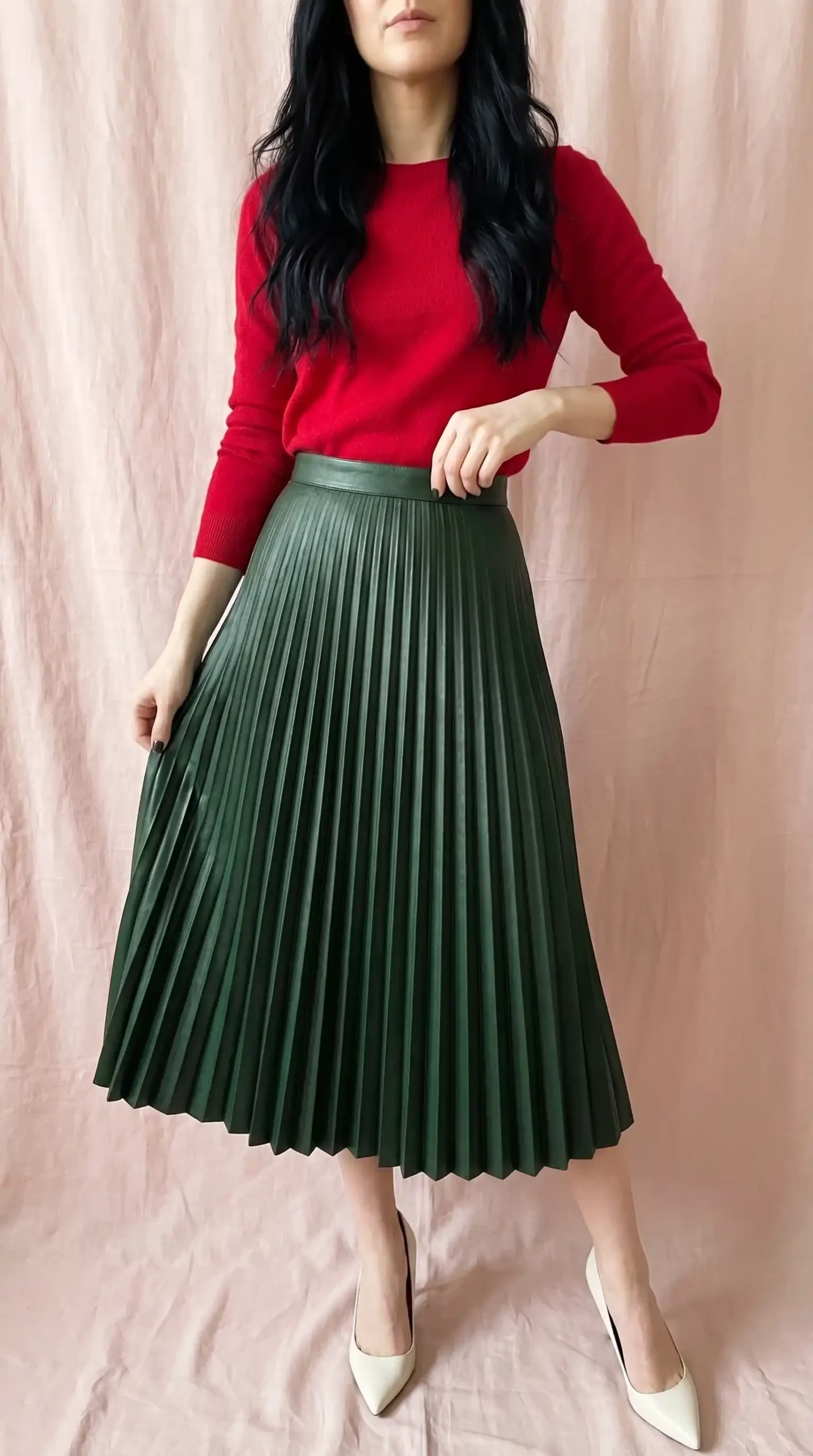 Woman in red ribbed knit sweater with dark green faux leather pleated midi skirt and white pumps