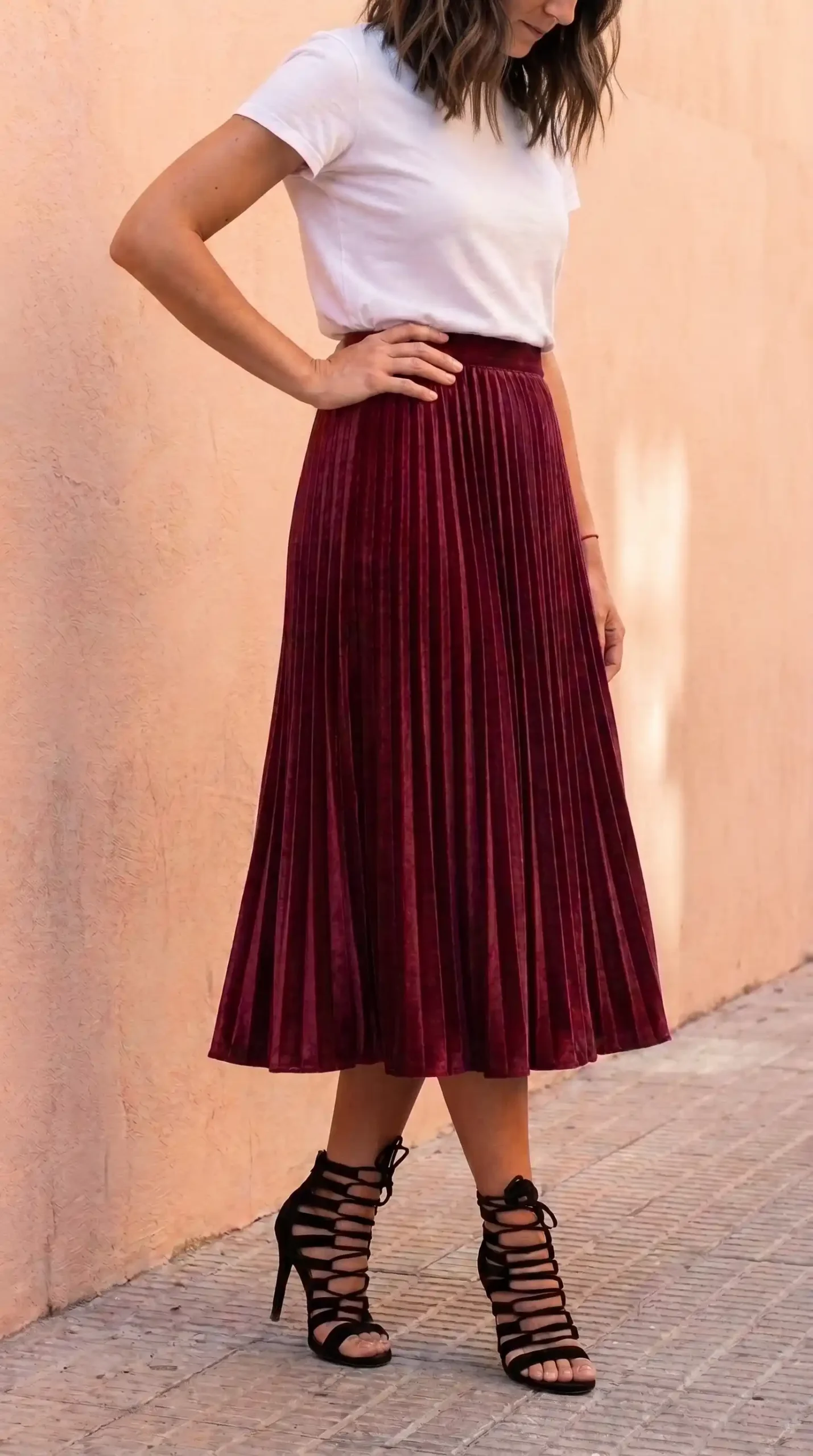 Woman in white crew neck tee with burgundy velvet pleated midi skirt and black lace up heels on sidewalk
