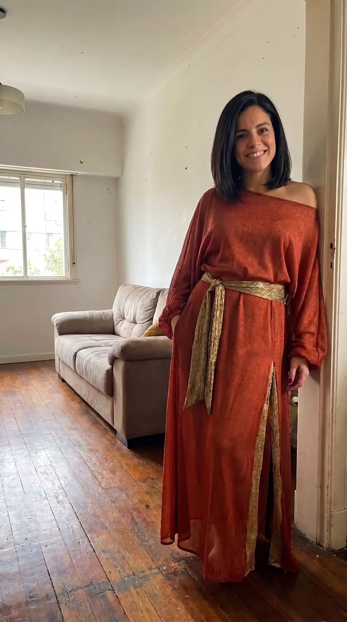 Woman dressed as Zuul from Ghostbusters in burnt orange rust one shoulder draped maxi dress with gold metallic wrap sash belt indoors