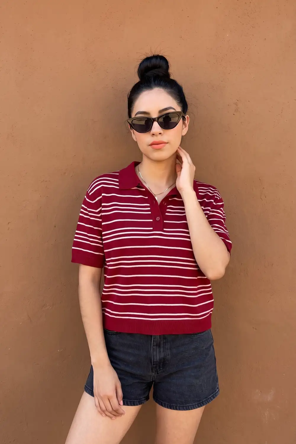 Woman in burgundy white stripe knit polo top with dark grey denim shorts