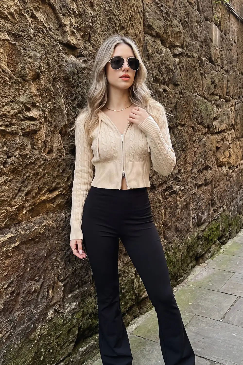 Woman in beige cropped cable knit zip-up cardigan with black high waist flare trousers