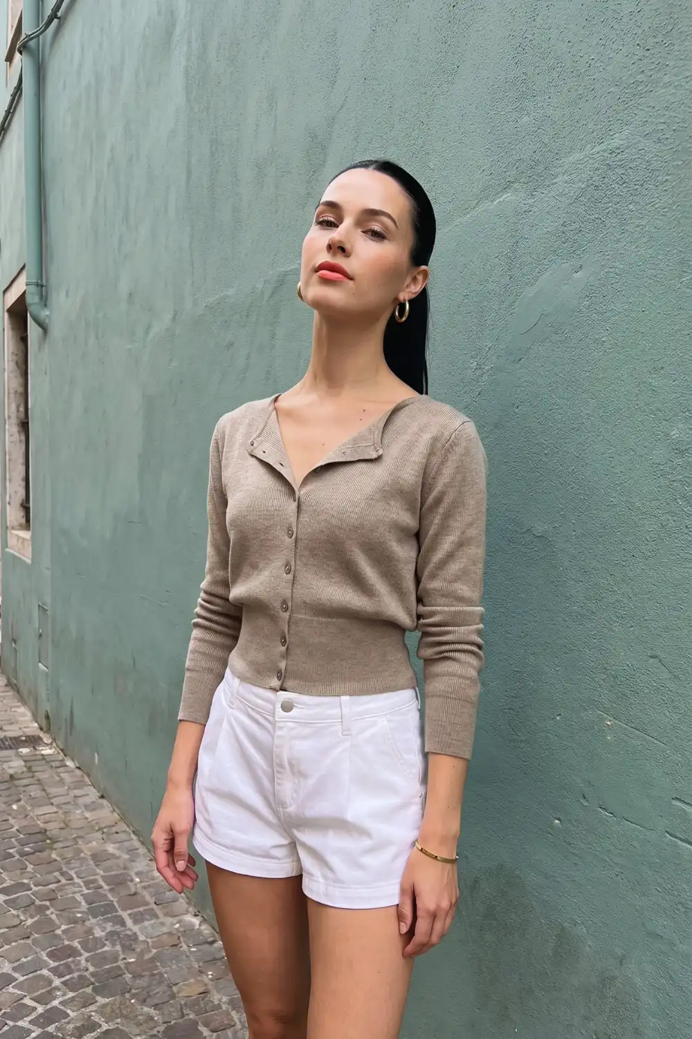 Woman in beige collared v neck fitted knit cardigan with white denim shorts