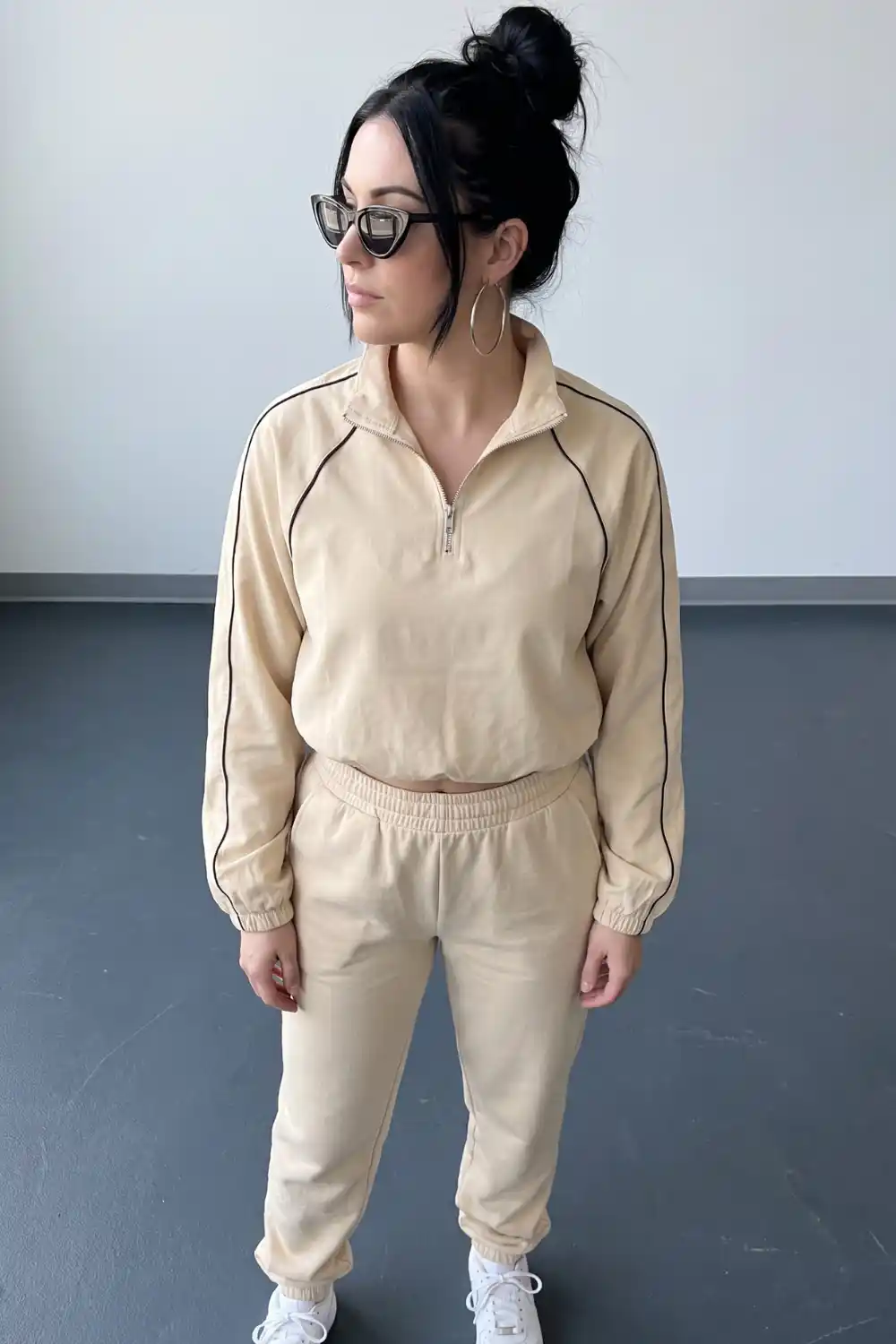 Woman wearing beige half-zip sweatshirt with black piping detail and matching joggers