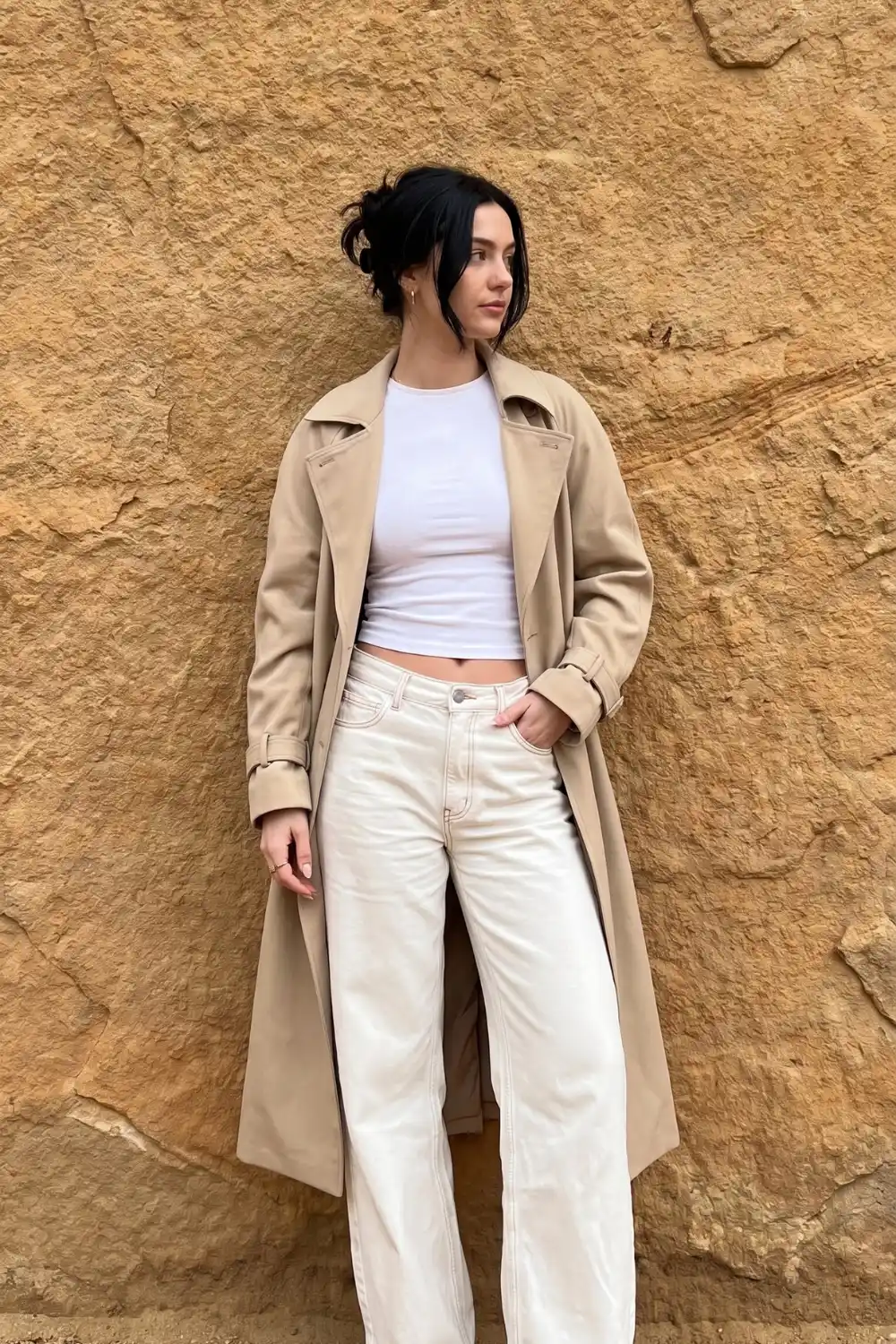 Woman wearing beige longline trench coat with white crop top and cream wide leg jeans