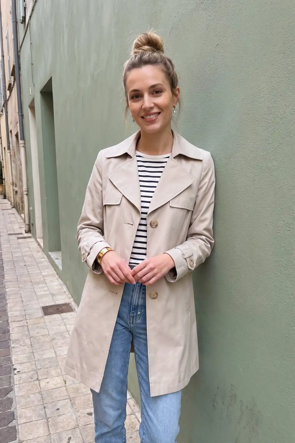 Woman in sand beige trench coat with navy white stripe top and light wash jeans