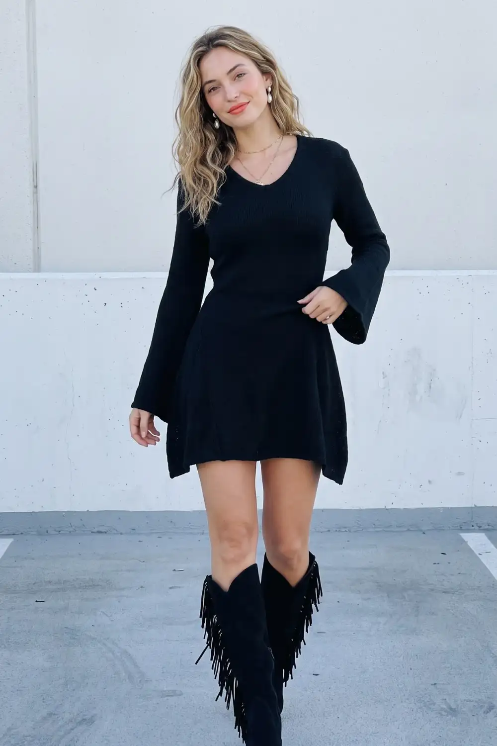 Woman in black v-neck bell sleeve sweater mini dress with black fringe knee high boots
