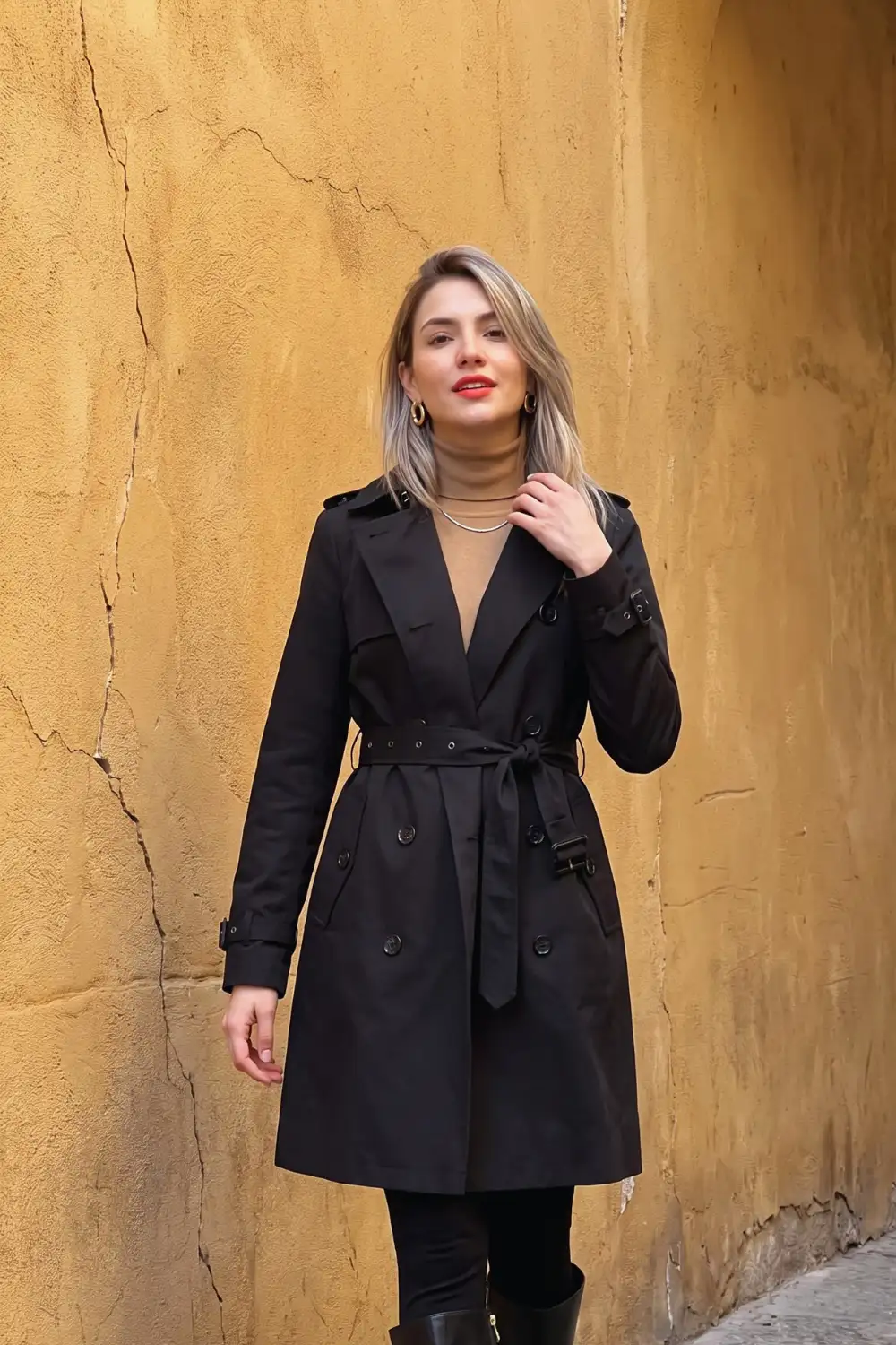 Woman in black belted double-breasted trench coat with camel turtleneck and knee high boots