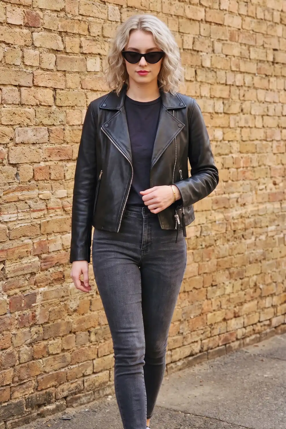 Woman in black leather biker jacket with silver zips and charcoal grey skinny jeans