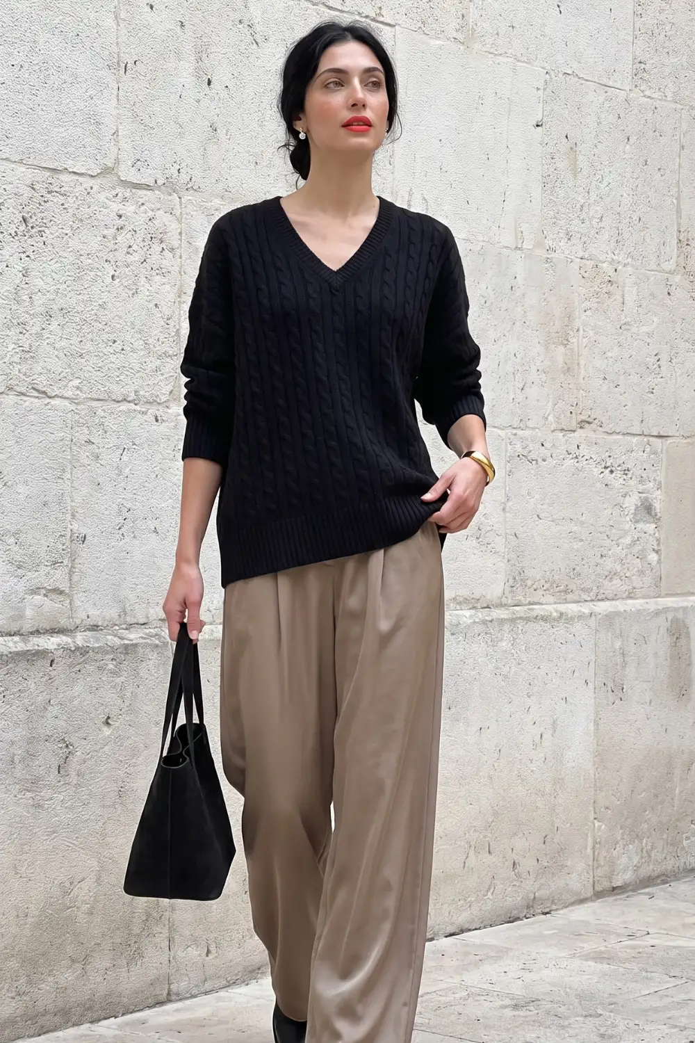 Woman in black cable knit v neck oversized sweater with taupe satin wide leg trousers