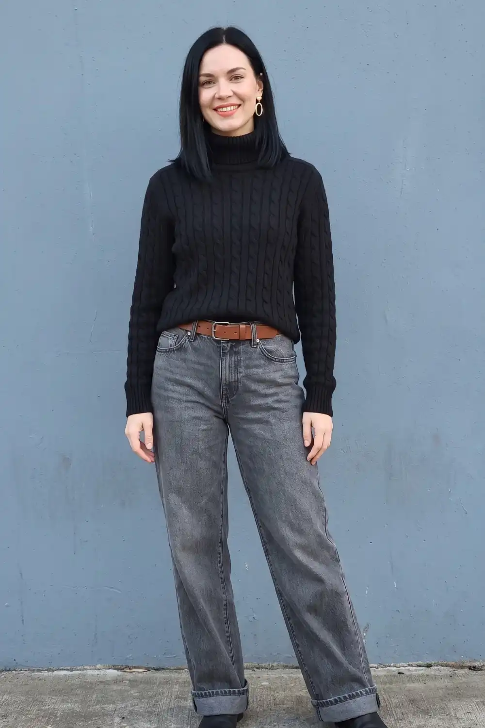 Woman in black cable knit turtleneck sweater with grey washed wide leg jeans and brown belt