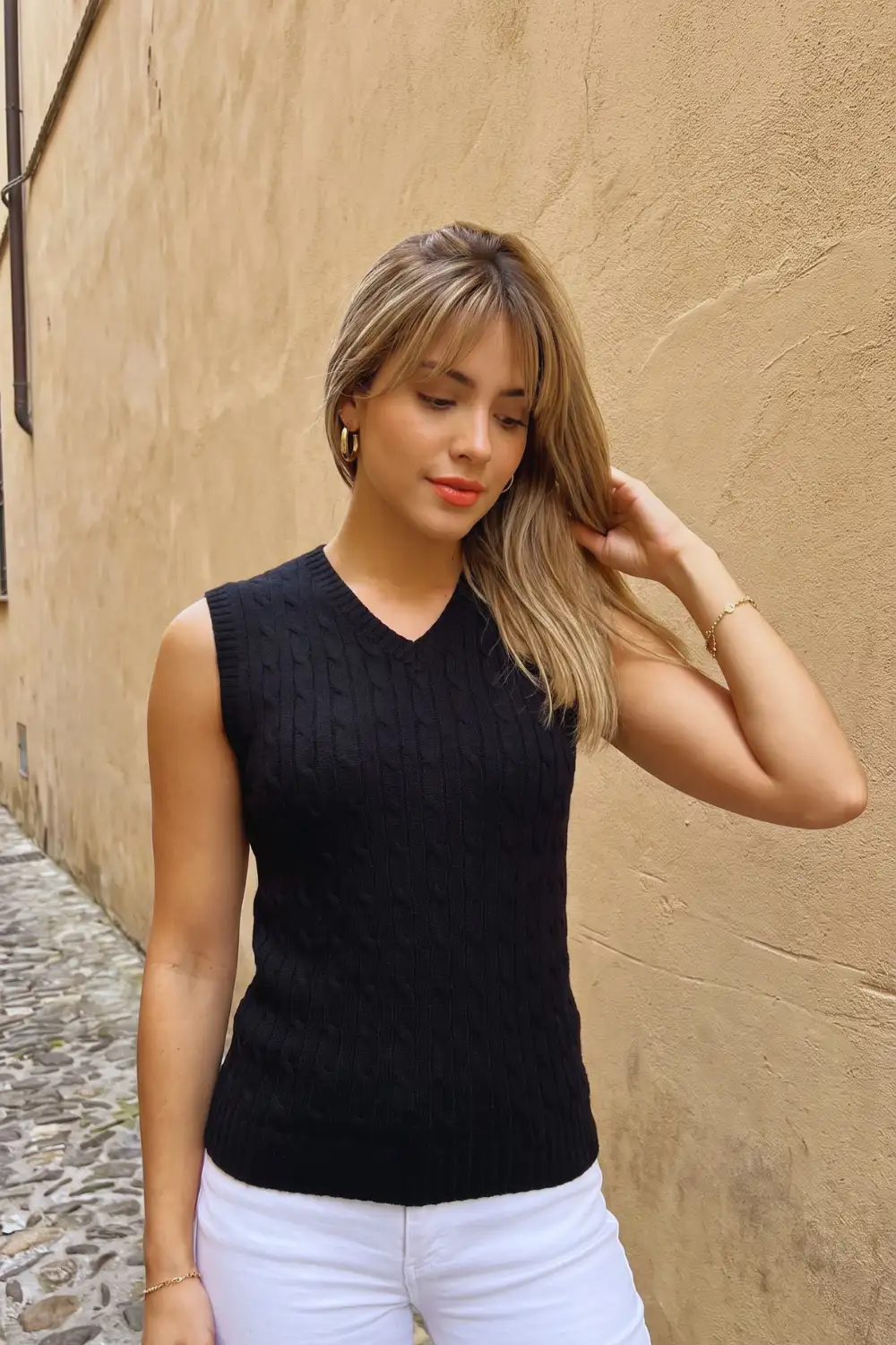 Woman in black cable knit v neck fitted sweater vest with white jeans