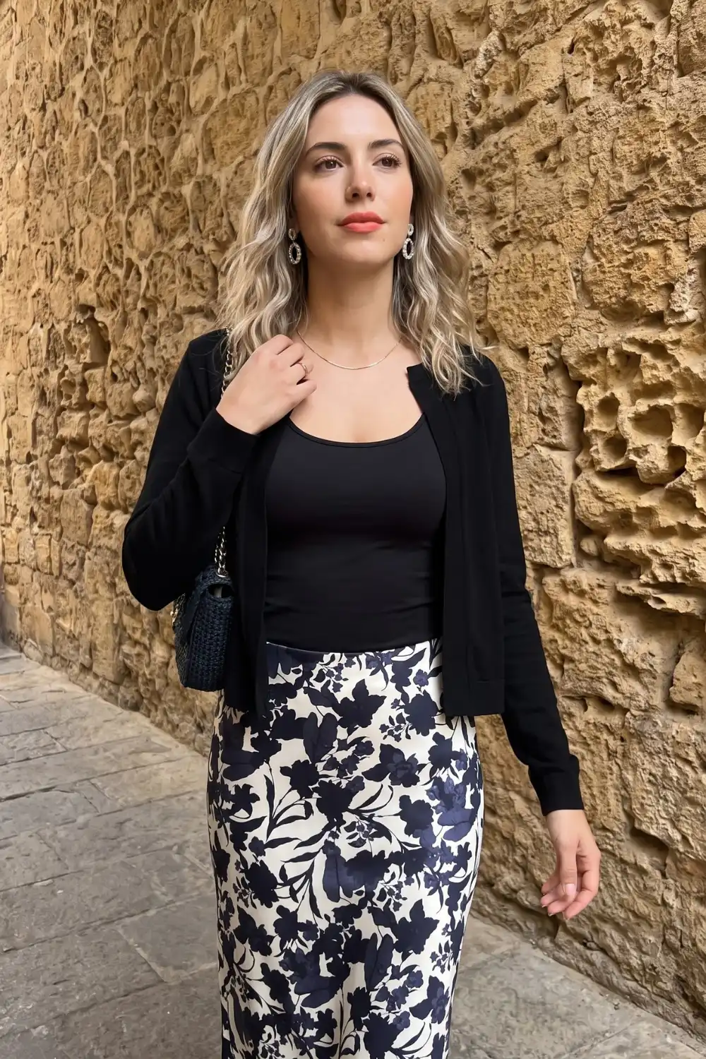 Woman in black cardigan and tank top with navy floral satin midi skirt