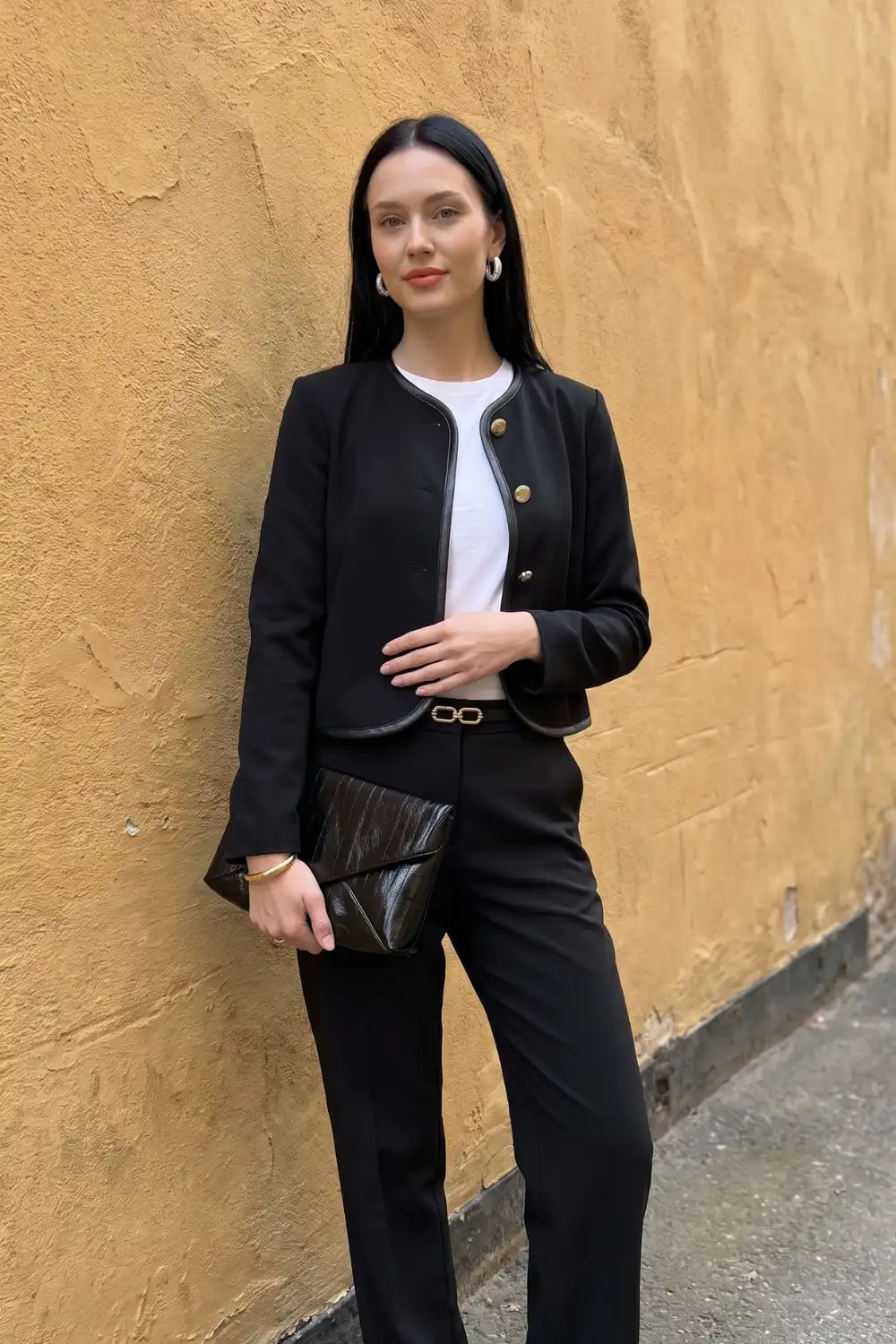 Woman in black collarless gold button blazer with white tee and black straight trousers