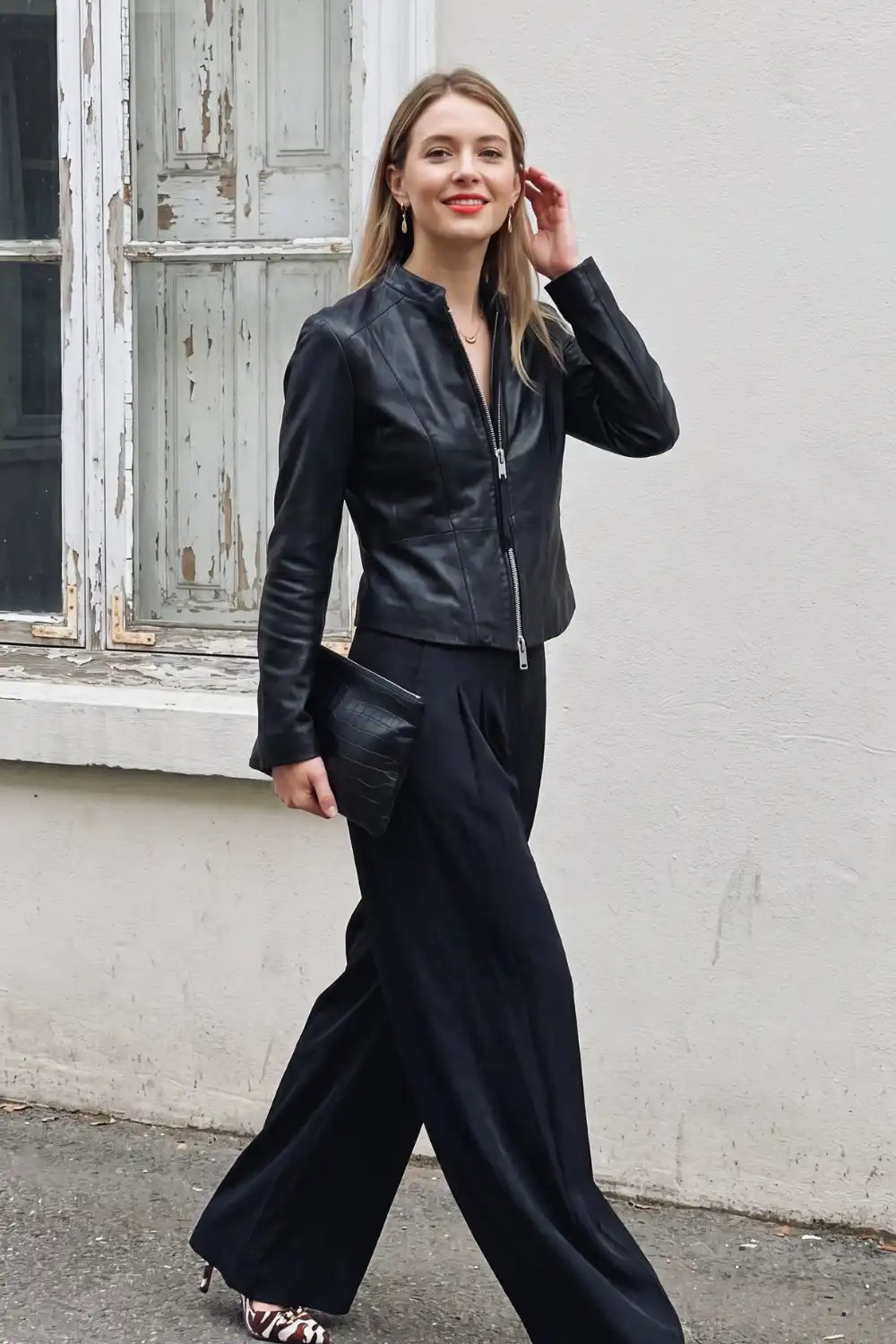 Woman in black collarless cropped zip-up leather jacket with black wide leg trousers