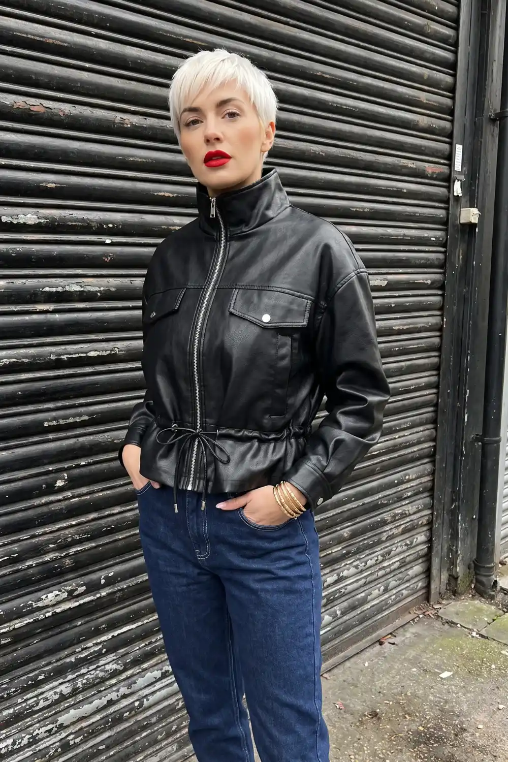 Woman wearing black drawstring waist zip up leather jacket with dark wash straight jeans