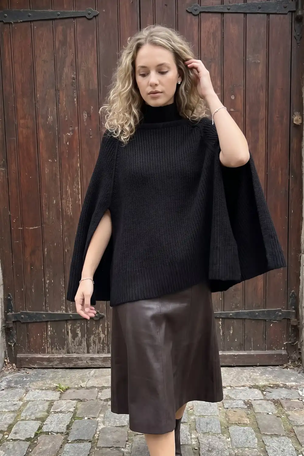 Woman in black chunky knit cape turtleneck with dark brown leather midi skirt