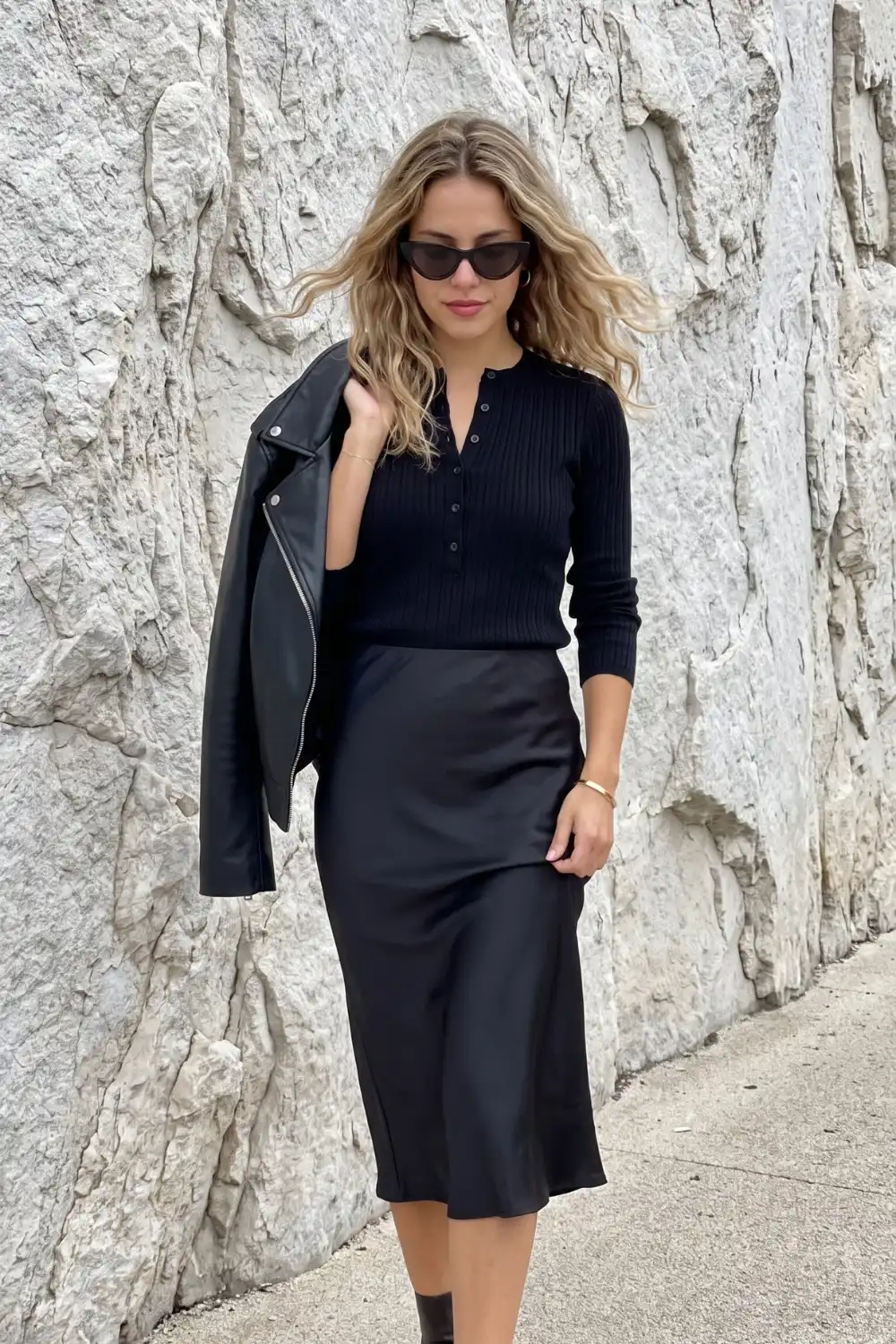 Woman in black ribbed henley knit top with black satin midi skirt and black moto jacket