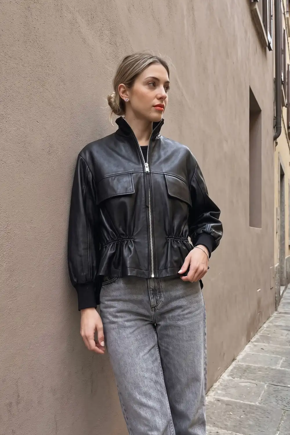 Woman in black leather zip-up bomber jacket with elasticated waist and grey straight jeans