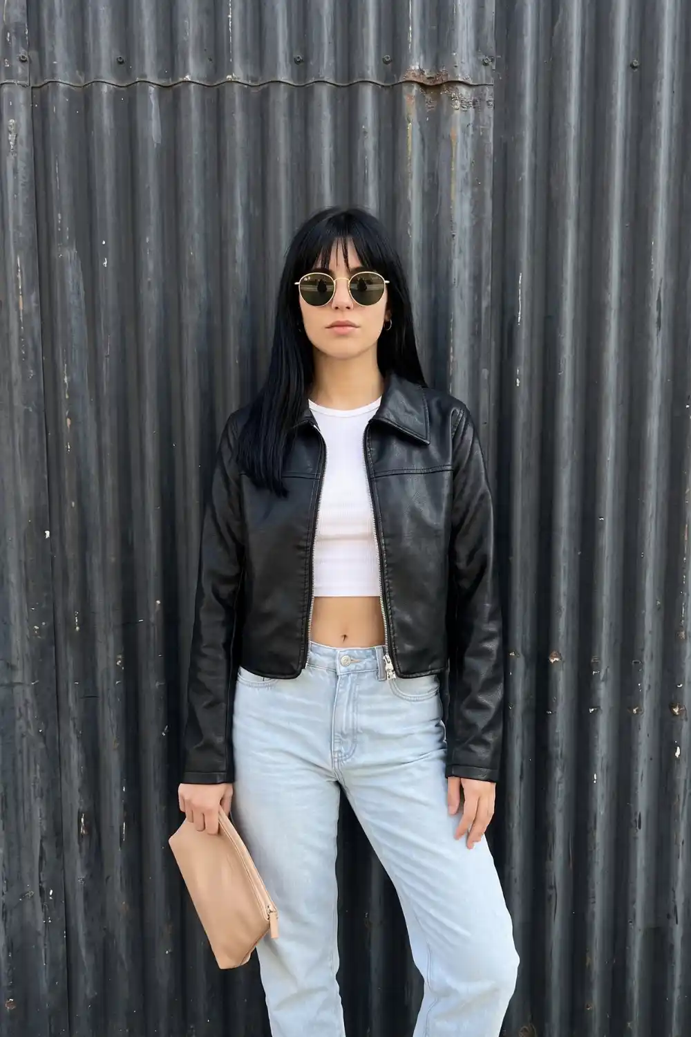 Woman wearing black zip up cropped leather jacket with white crop top and light wash straight jeans