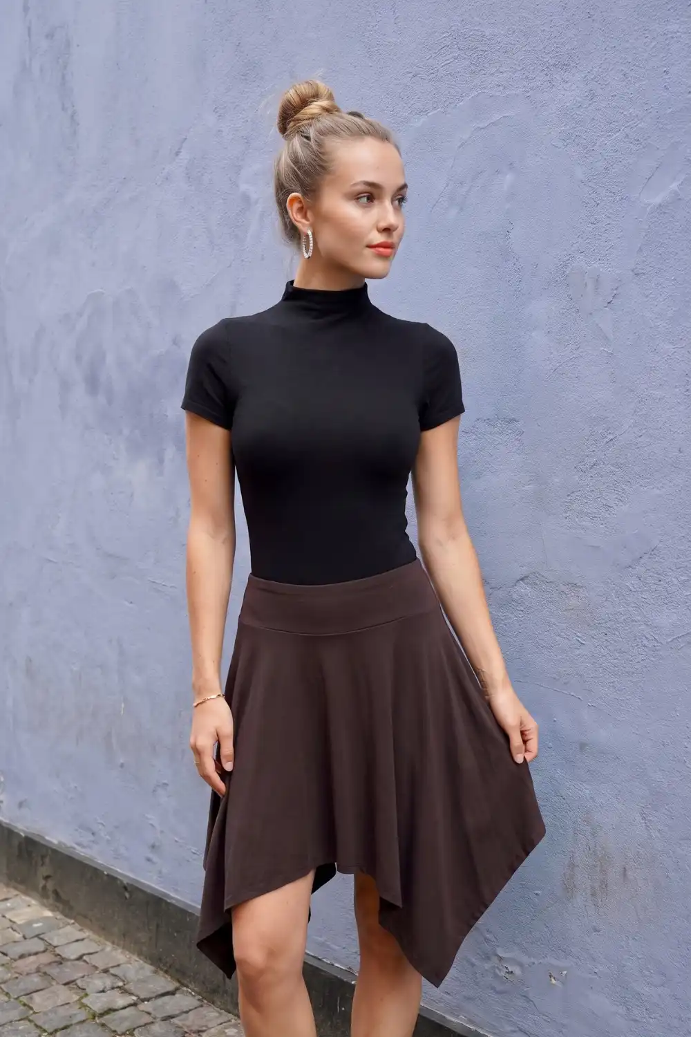 Woman in black short sleeve mock neck top with dark brown asymmetric flared mini skirt
