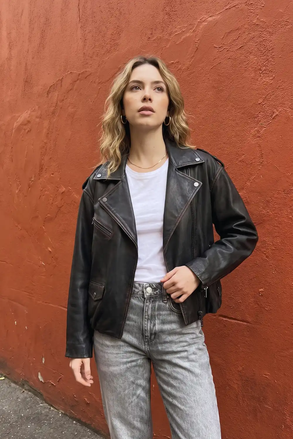 Woman in black oversized moto leather jacket with white tee and light grey straight jeans