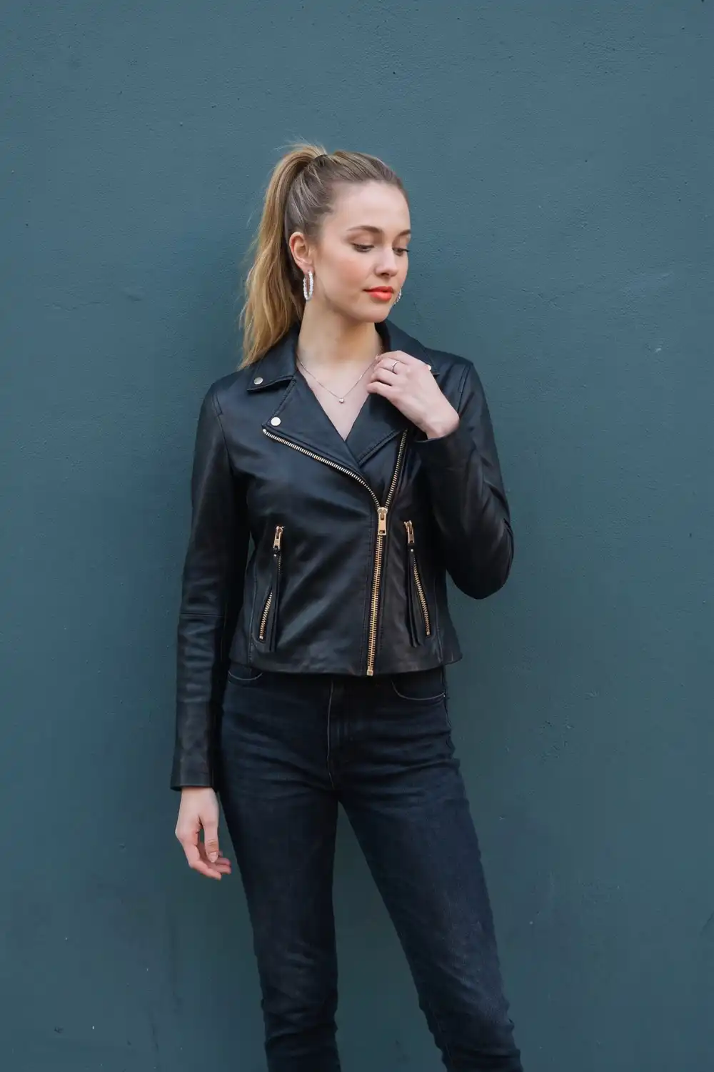 Woman in black leather moto jacket with gold zips and dark wash skinny jeans