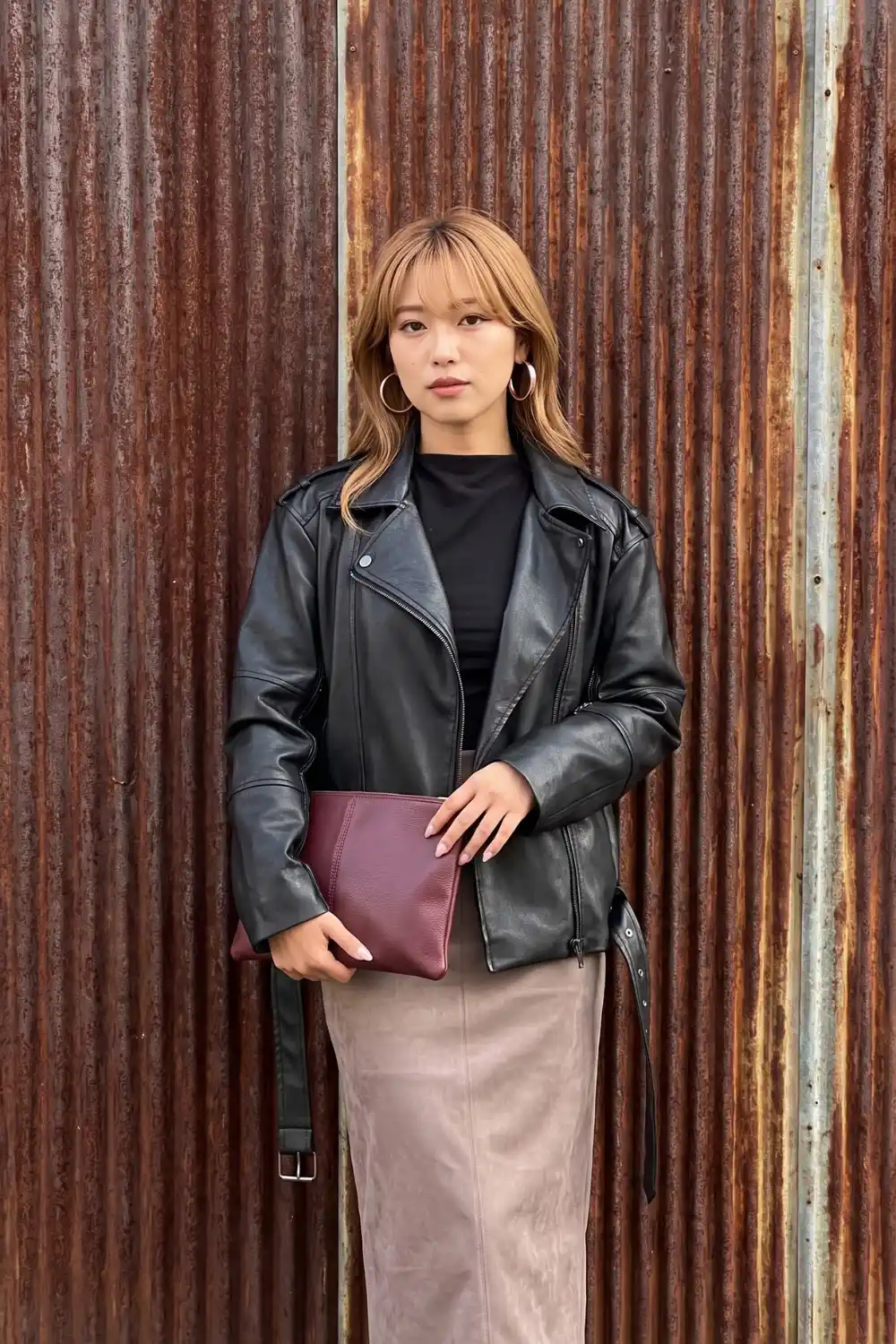 Woman wearing black oversized moto leather jacket with black top and dusty pink suede midi skirt