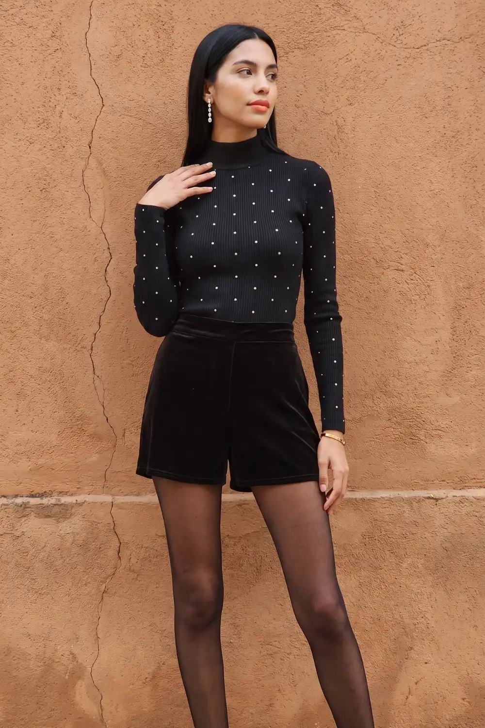 Woman in black pearl embellished turtleneck top with black velvet shorts and tights