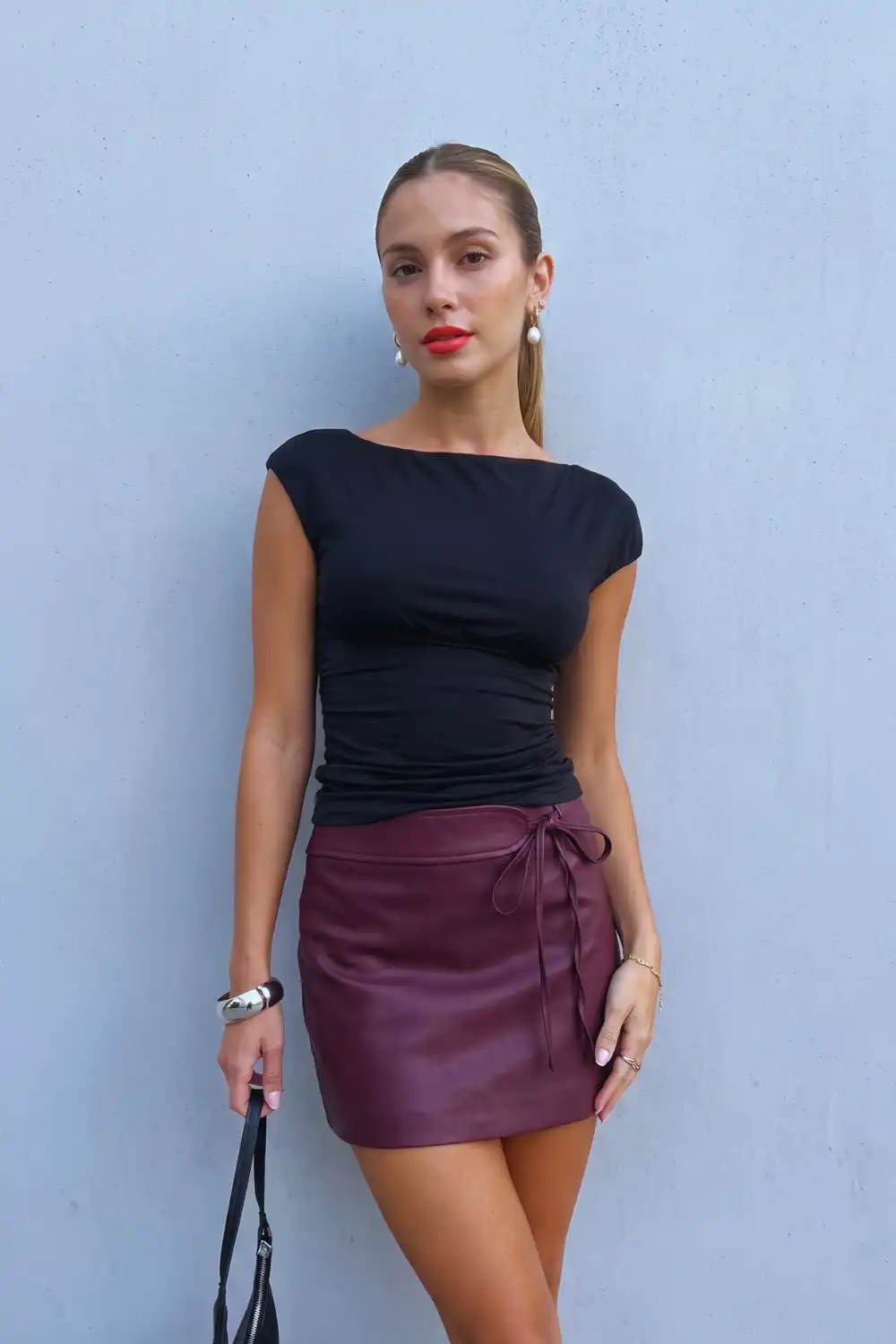 Woman in black ruched boat neck top with burgundy leather tie wrap mini skirt